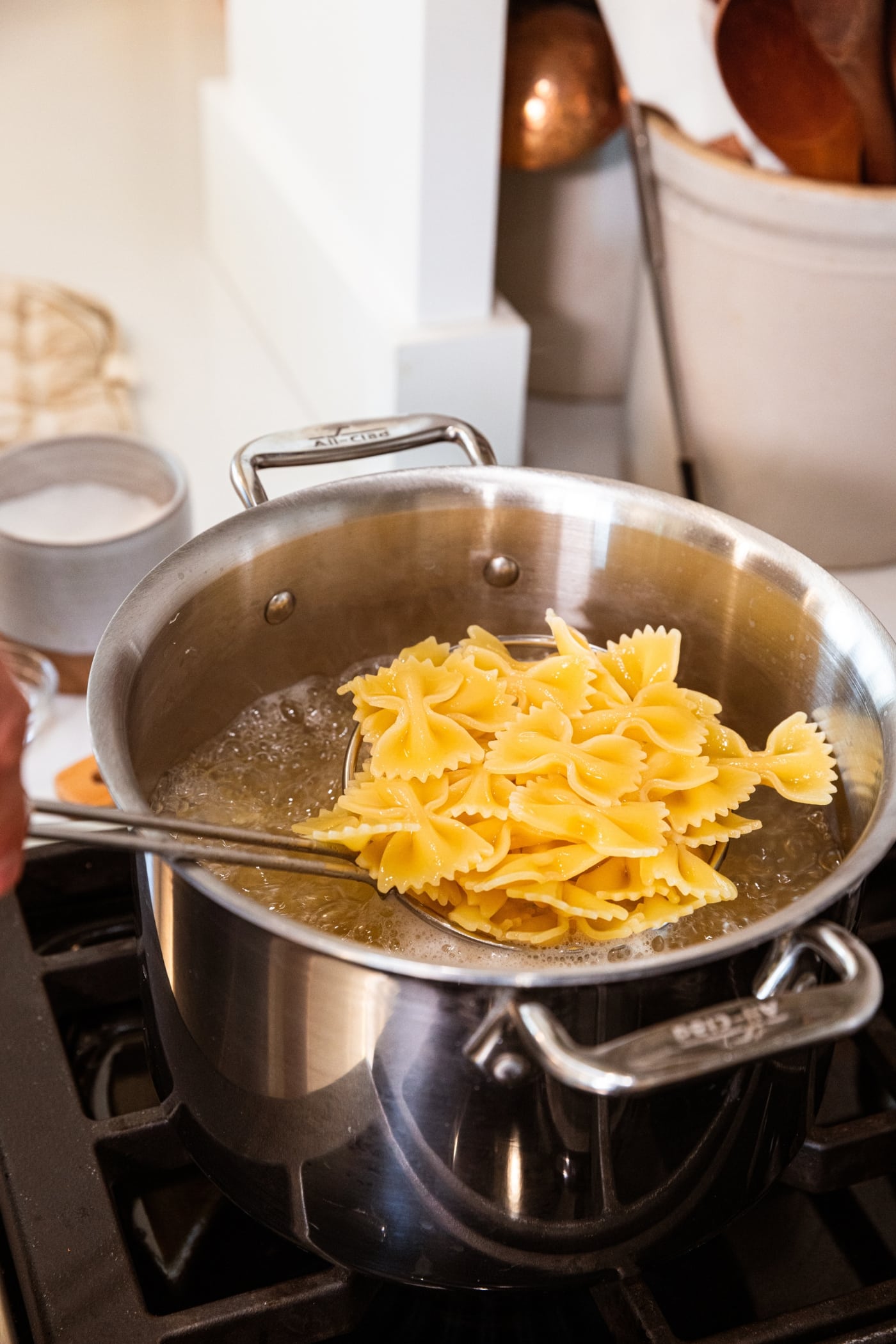 Hand holding spider with cooked pasta above large stockpot filled with water after cooking.