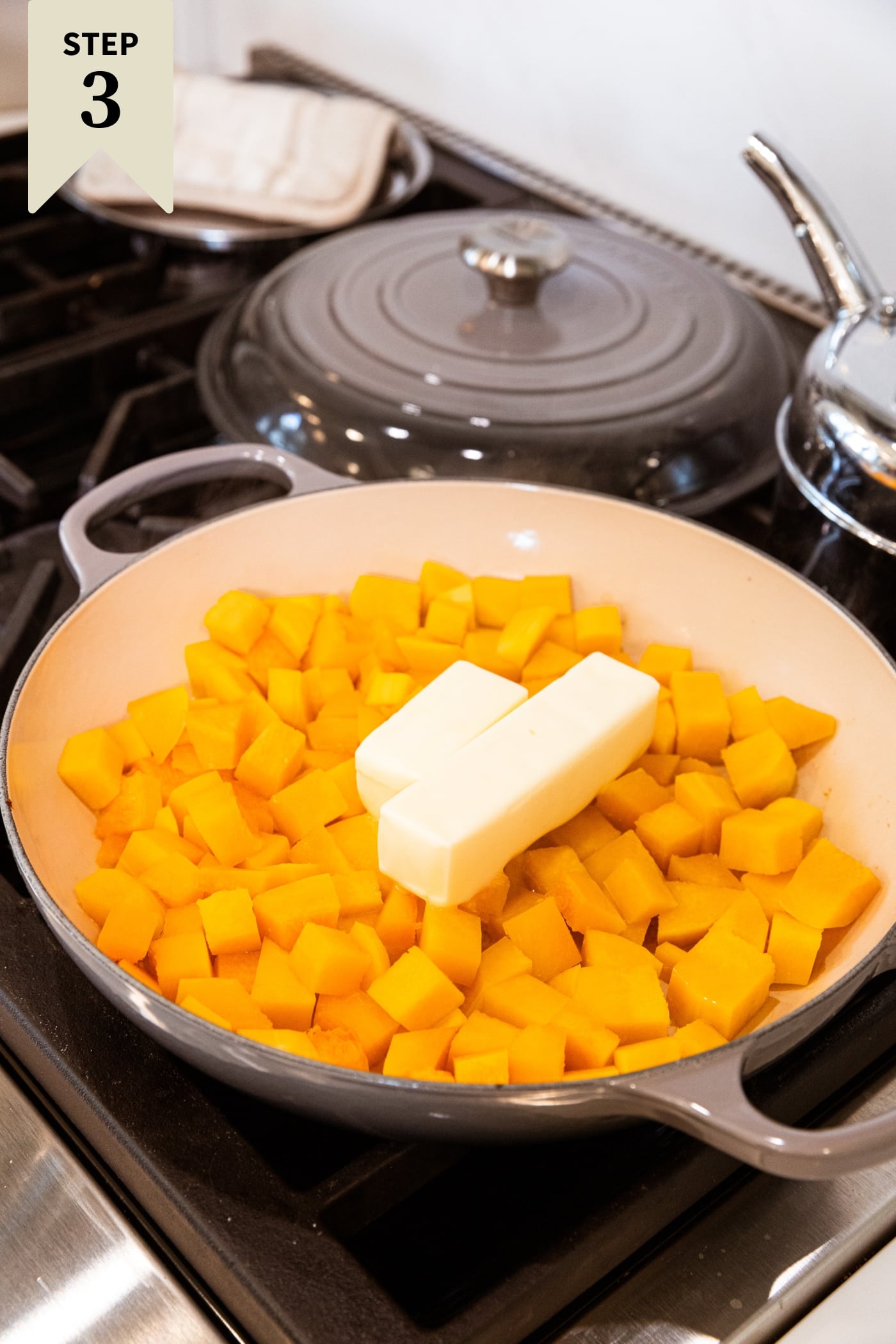 Large gray skillet filled with cooked butternut squash cubes with butter about to melt on top all on stovetop.