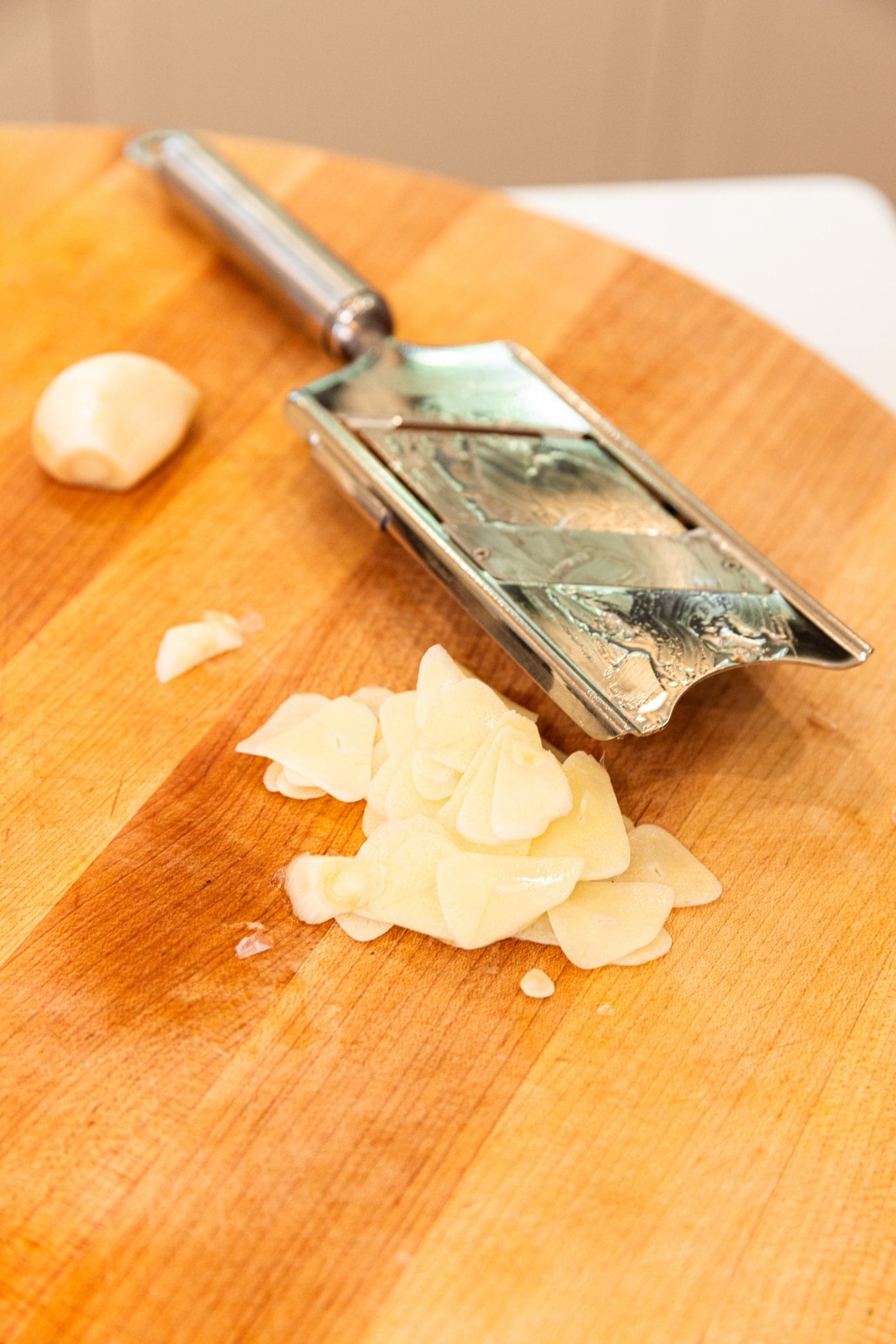 Sliced pieces of garlic with small slicer resting on wooden cutting board.