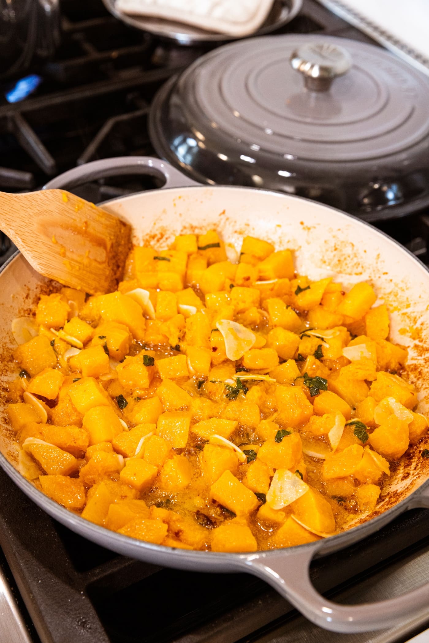 Wooden spatula mixing together cubed cooked butternut squash with herbs, butter, and garlic.