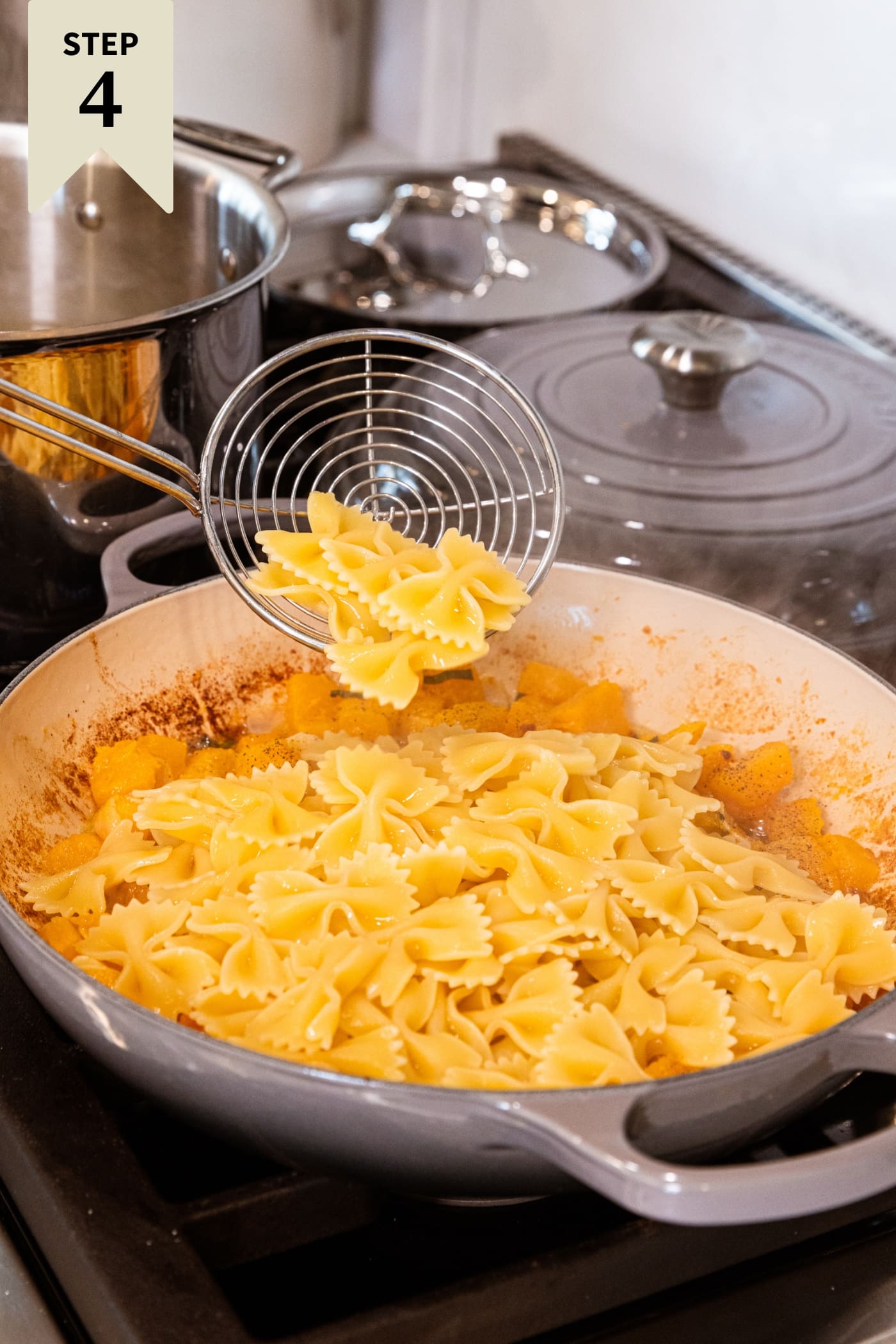 Spider holding cooked pasta dumping in on top of cooked butternut squash with browned butter.