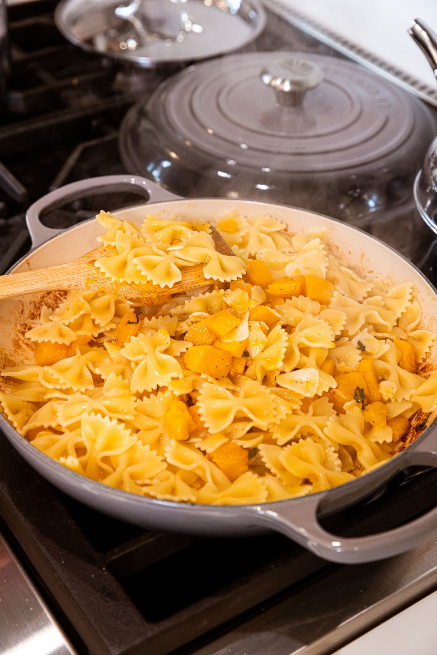 Wooden spatula mixing together cooked pasta with butternut squash and browned butter.