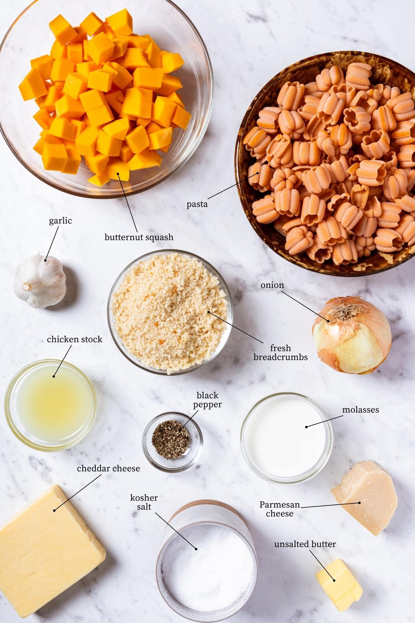White marble surface filled with all ingredients needed to prepare butternut squash pasta including pasta, onion, spices, stock, and more.
