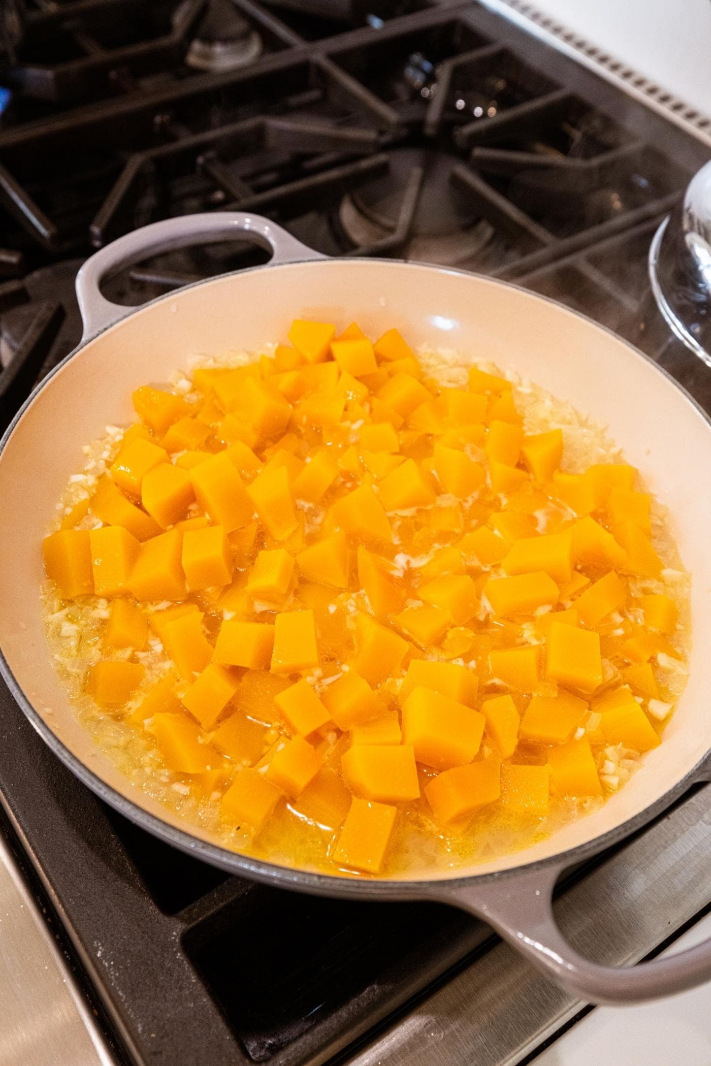 Large pot on the stovetop with cooked cubes of butternut squash in liquid.