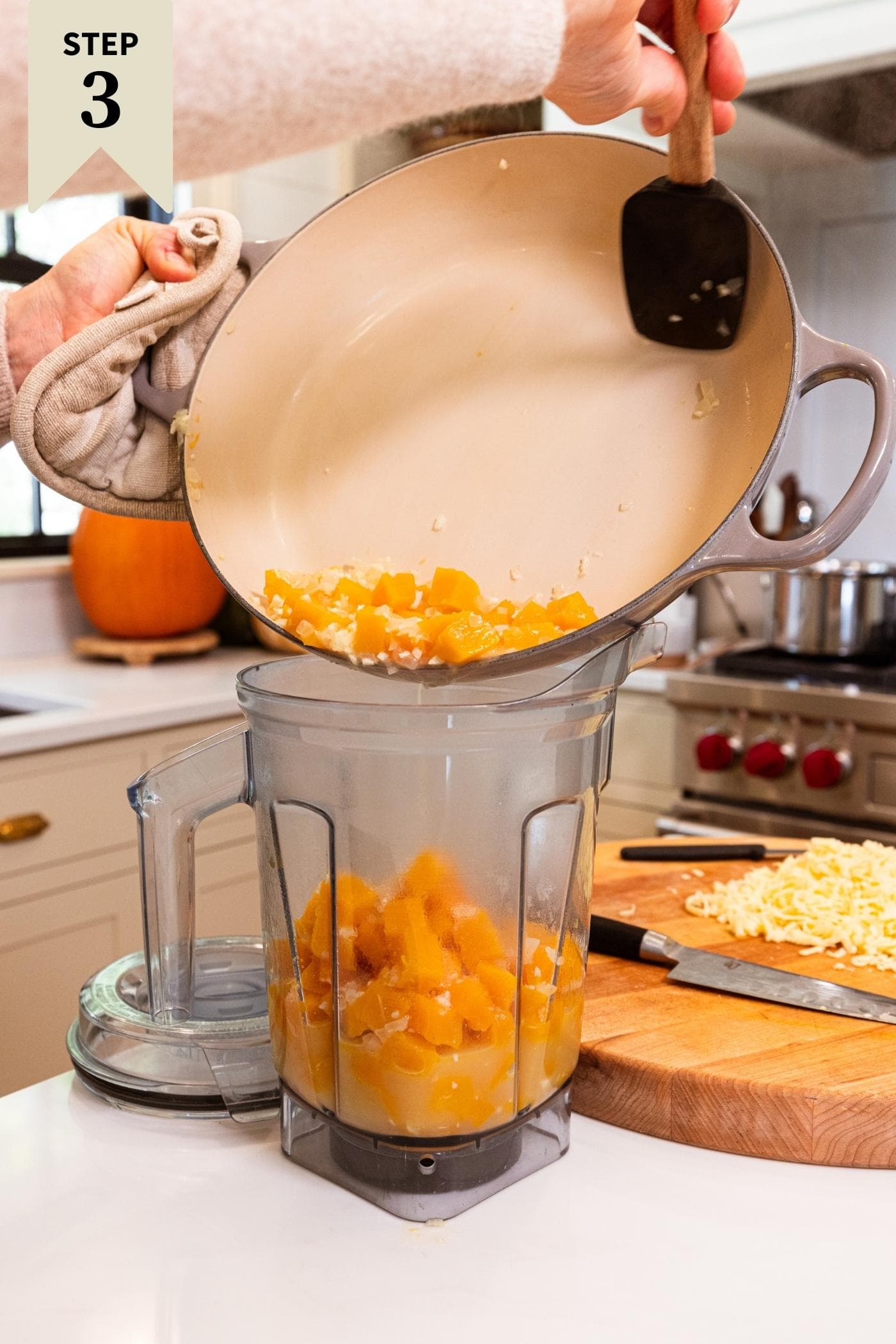 Hands holding large pot filled with cooked pieces of butternut squash pouring into canister blender.