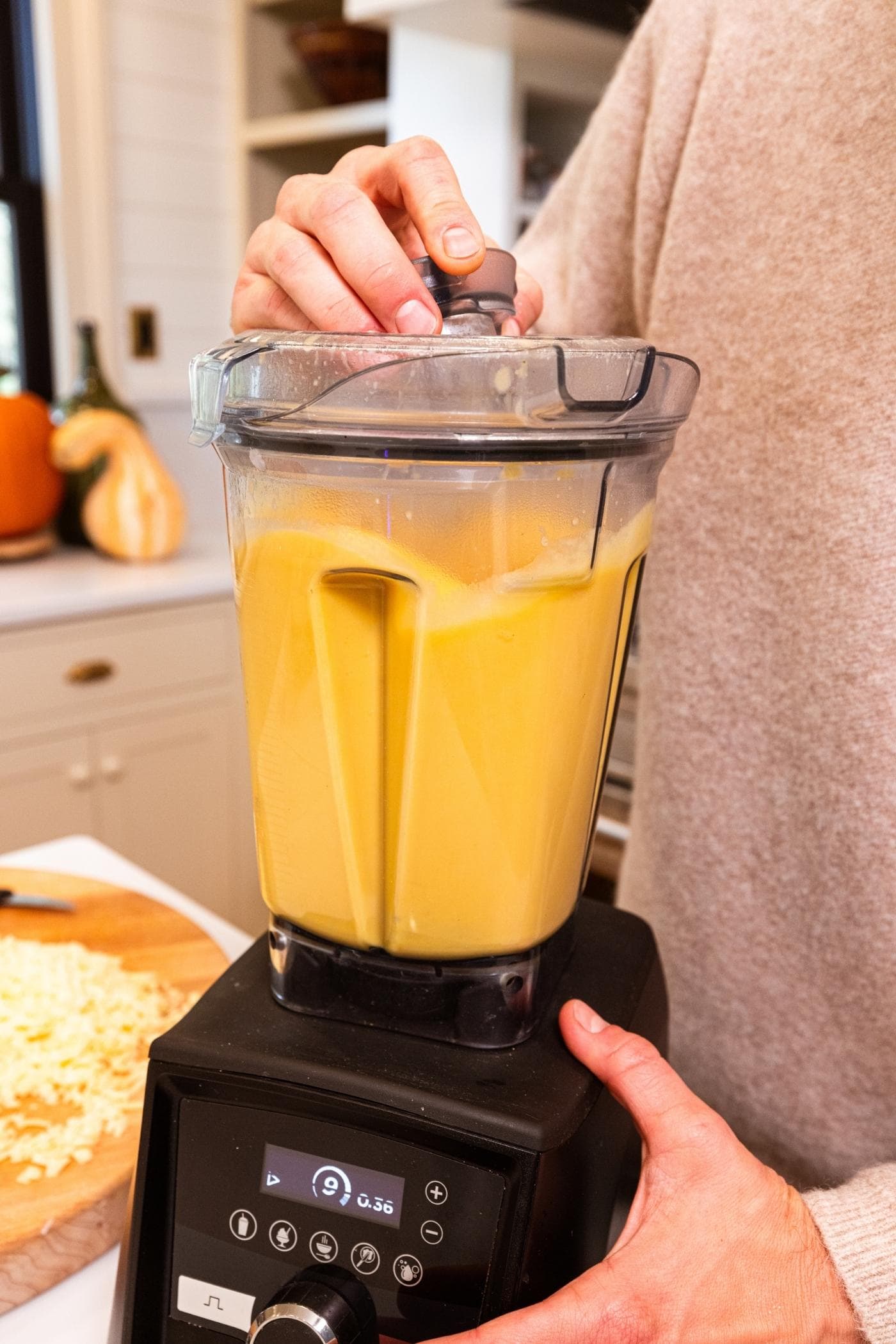Canister blender blending up pieces of butternut squash to form an orange smooth liquid.