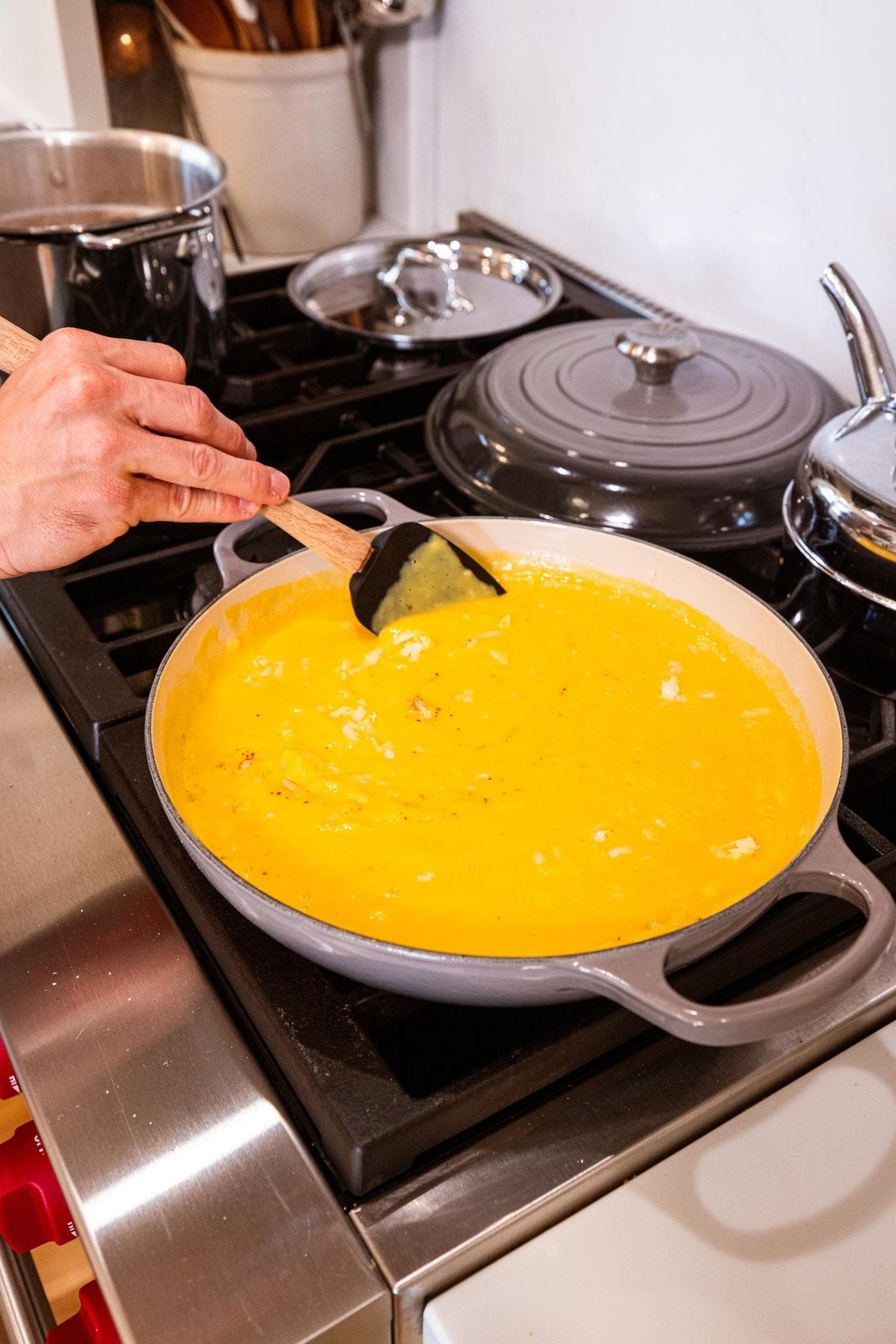 Spatula mixing together cheese and spices with smooth butternut squash sauce in large pot on stove.