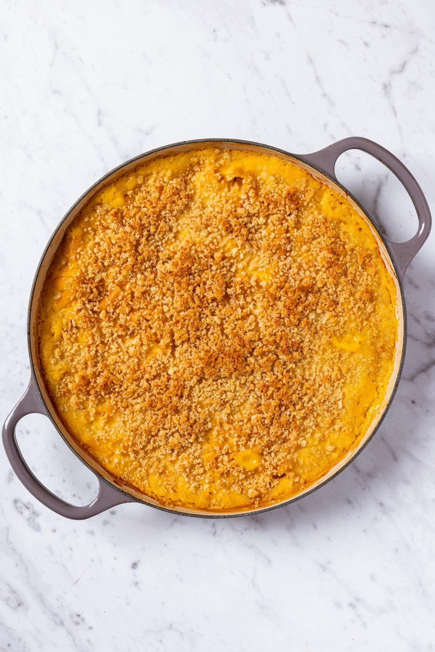 Large pot sitting on marble surface with cheesy butternut squash pasta after being baked in the oven.