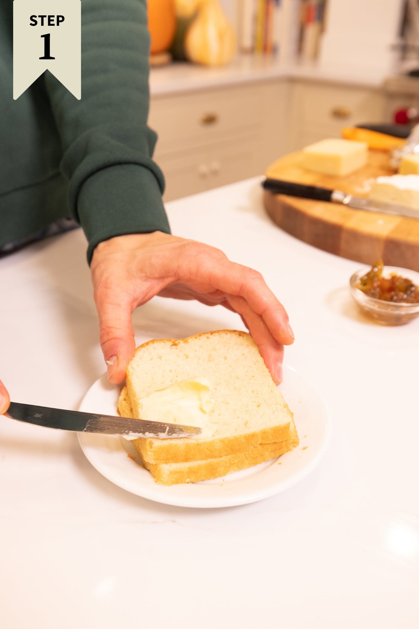 Hand using a knife to spread butter on top of two slices of white bread.