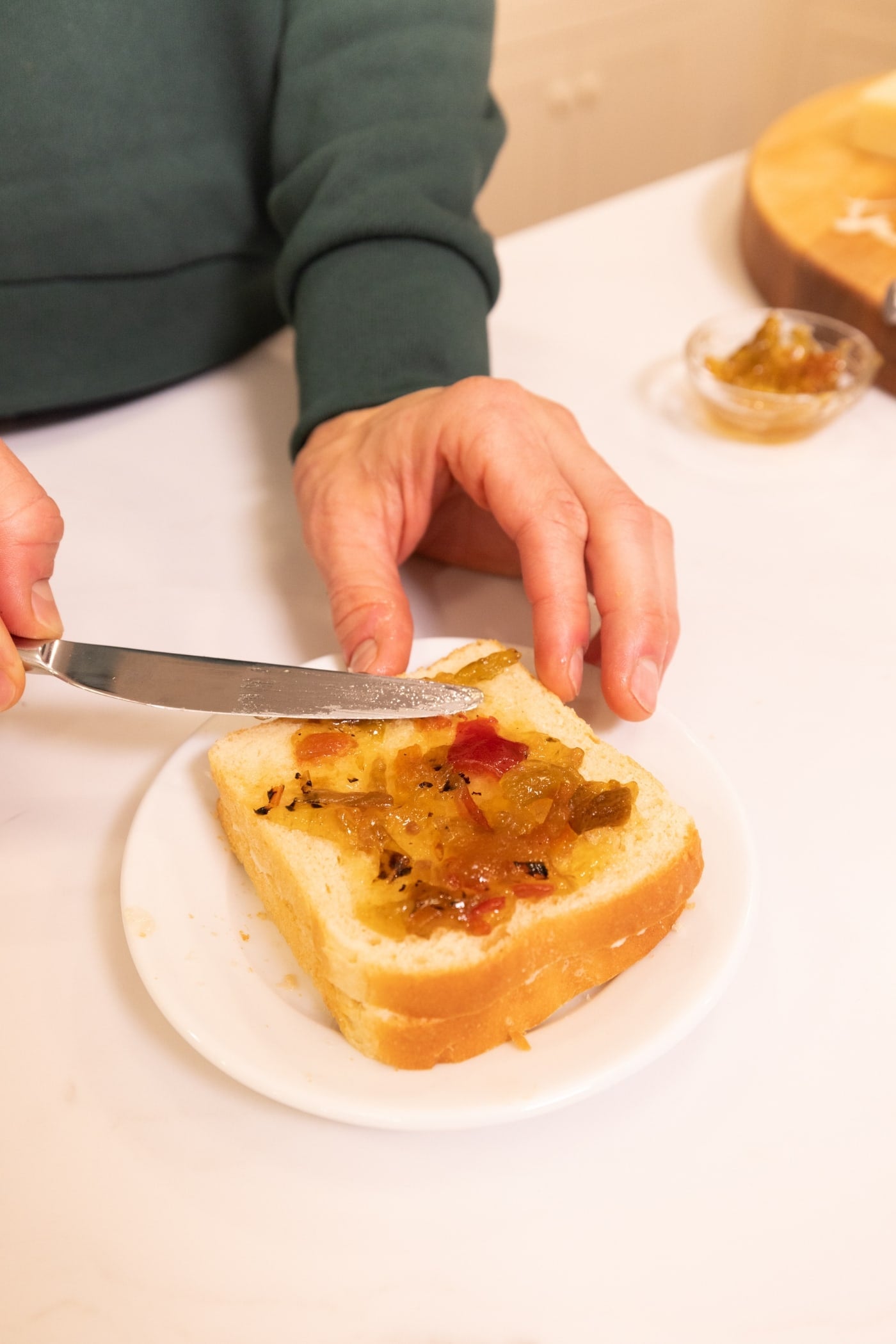 Knife spreading pepper jam onto a slice of buttered white bread.