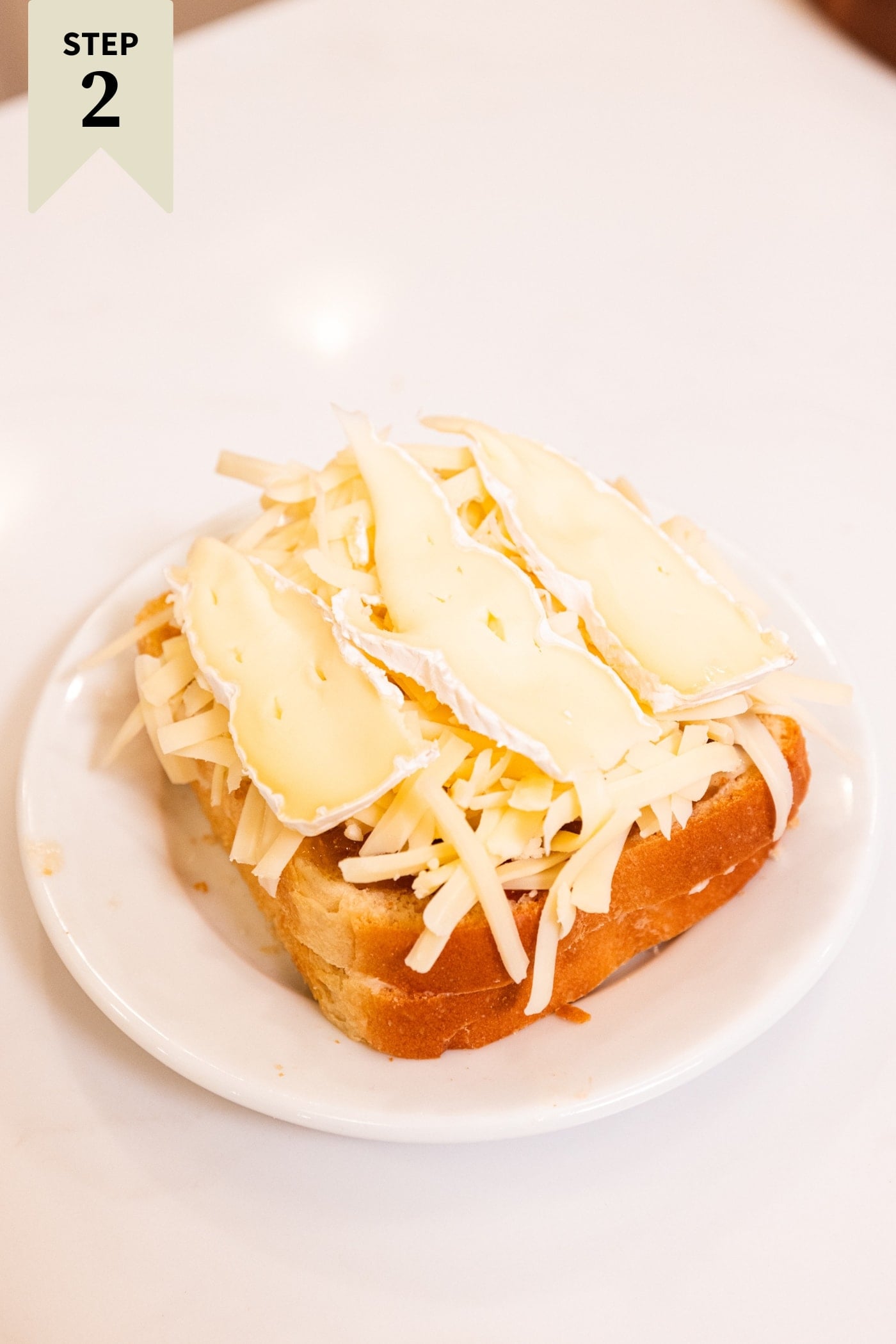 Slices of bread layered with shredded and sliced cheese on top sitting on a white plate.