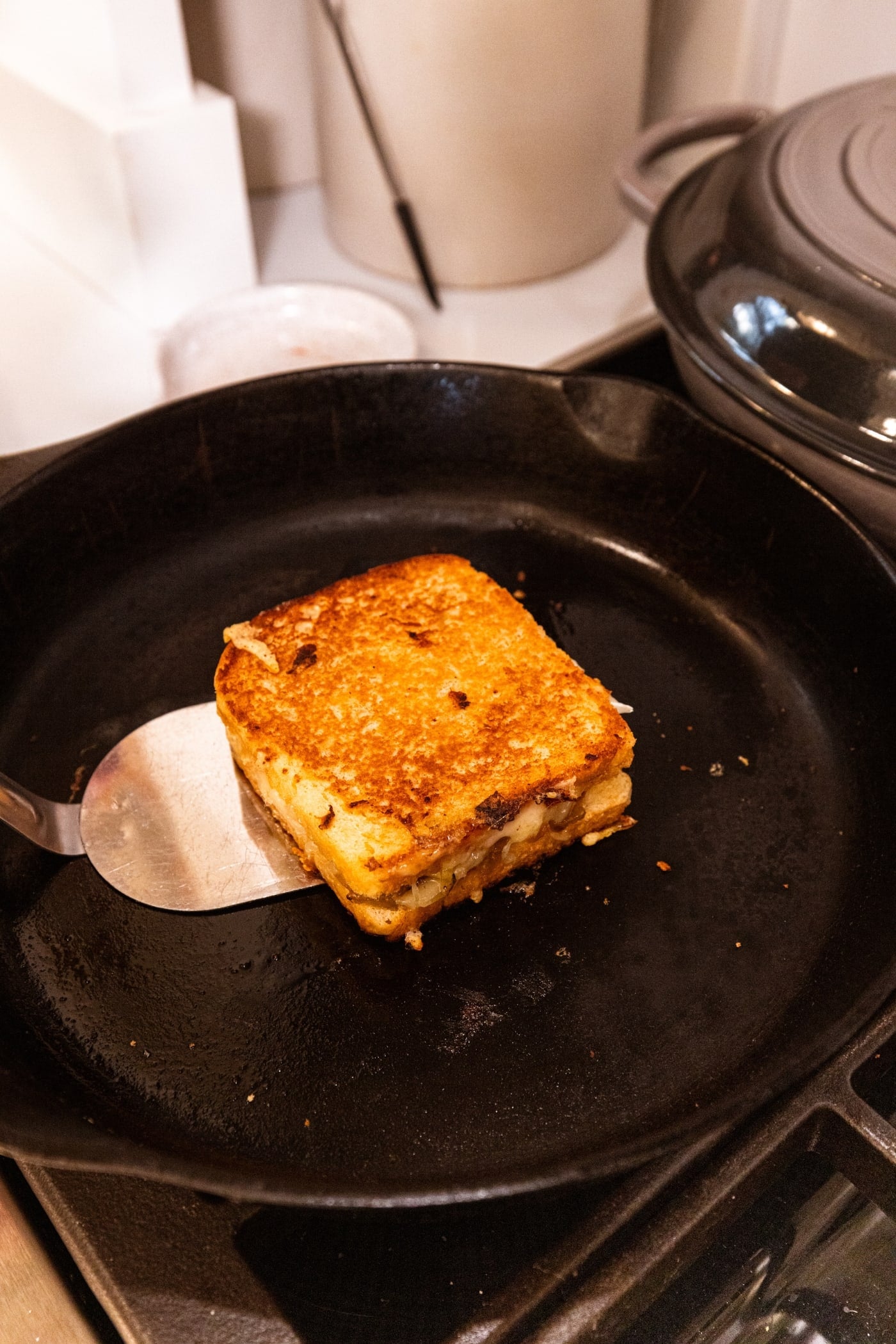 Metal spatula about to flip over a grilled cheese sandwich that was browned in a large black skillet.