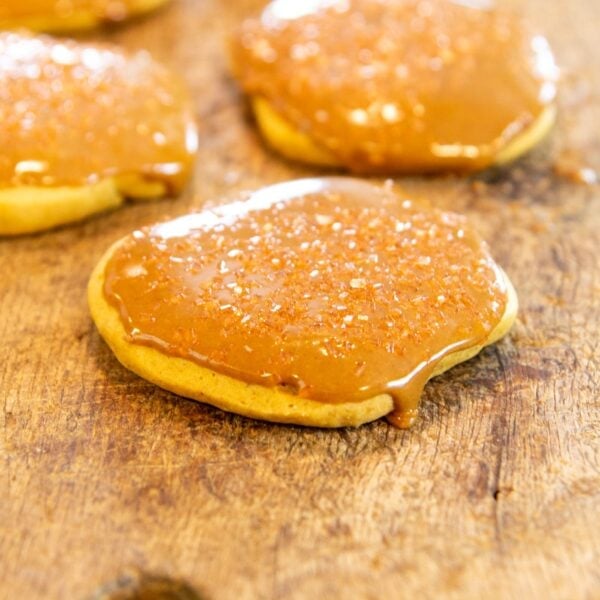 A cookie with a glaze sits on a wooden board.