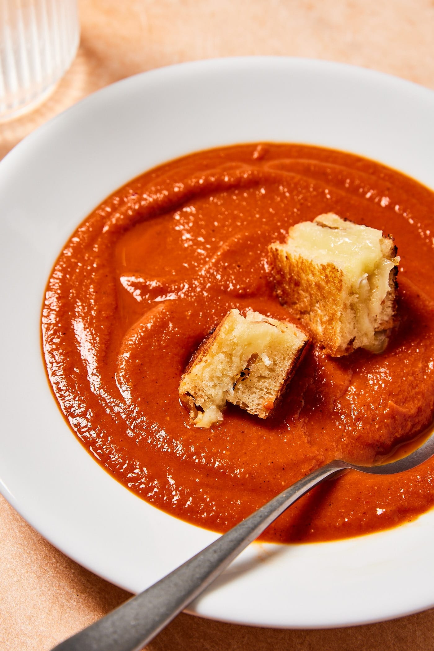 White bowl filled with roasted tomato soup with large grilled cheese croutons sitting in soup.