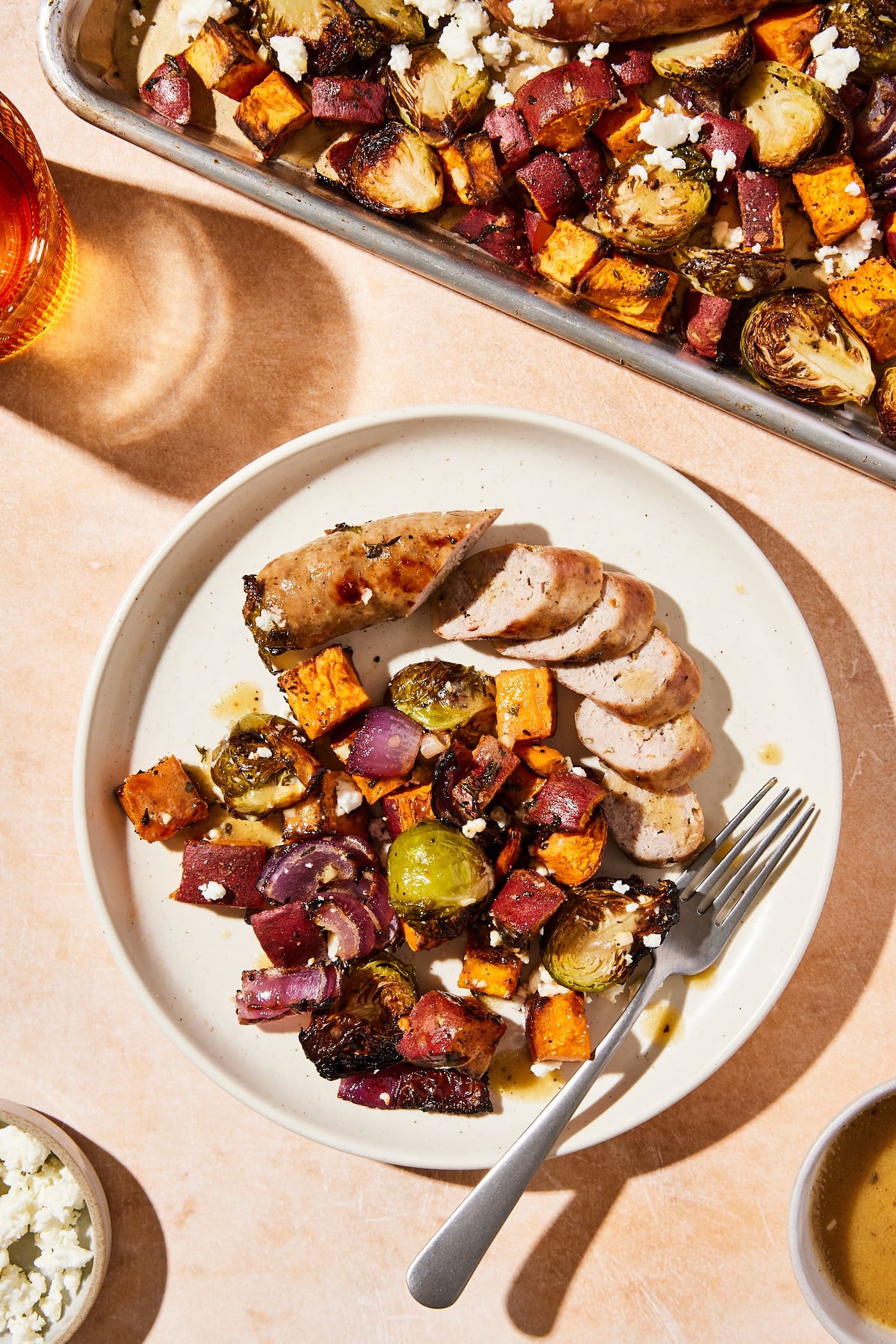White plate with serving of sheet pan sausage and roasted vegetables with glass of water to the side.