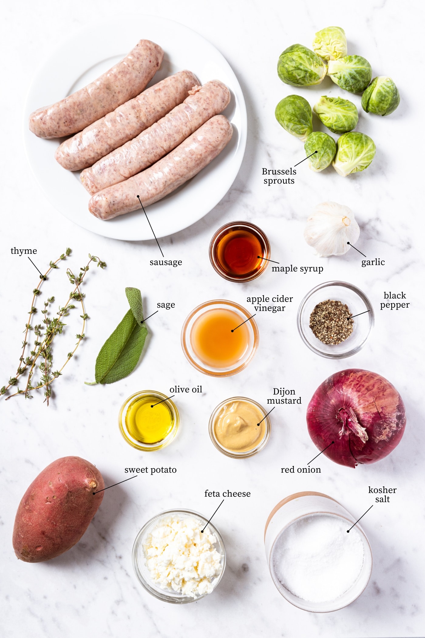 White marble surface filled with all ingredients needed to make sheet pan sausage including spices, sausage, vegetables, and more.