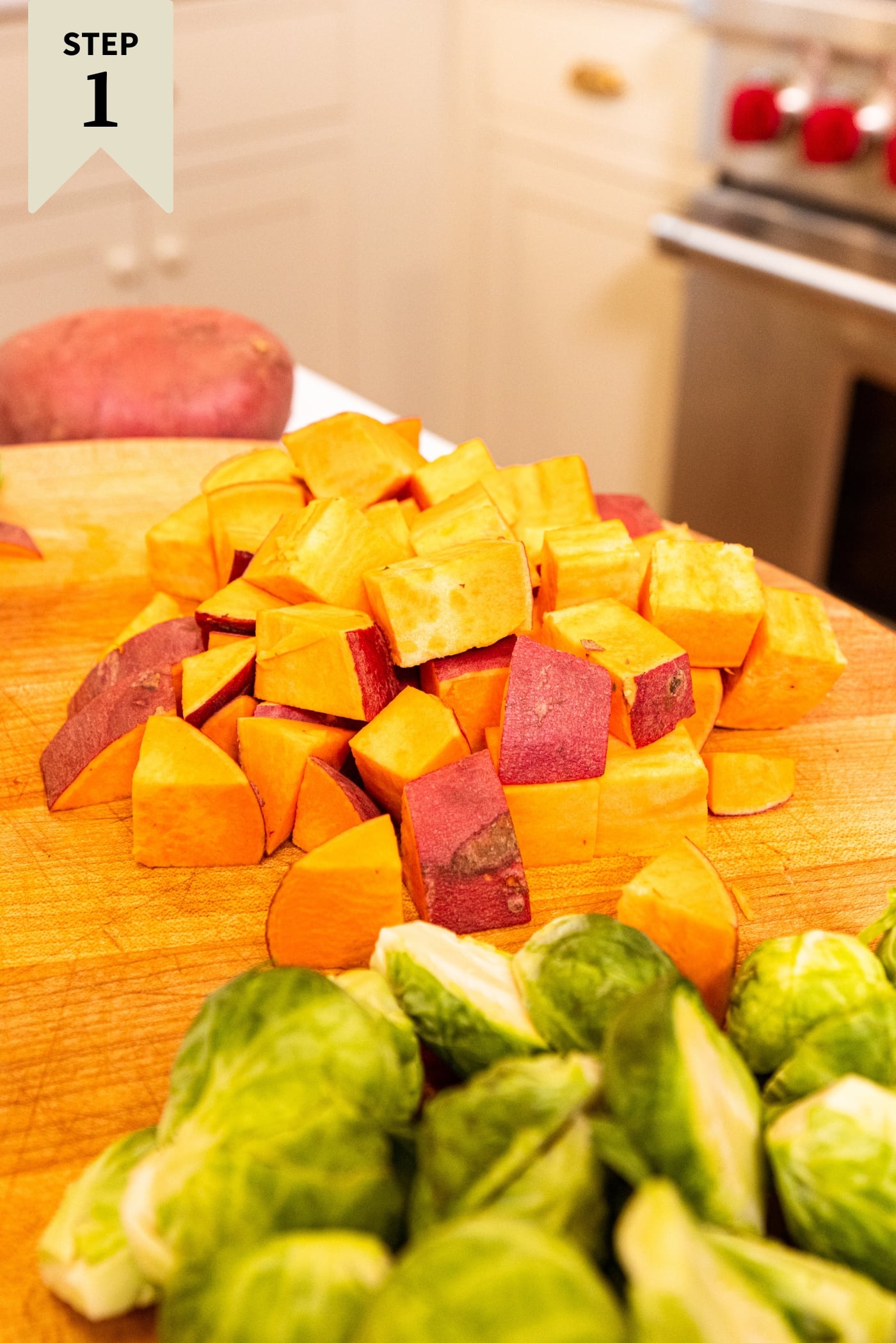 Wood cutting board with chopped sweet potatoes and Brussels sprouts.
