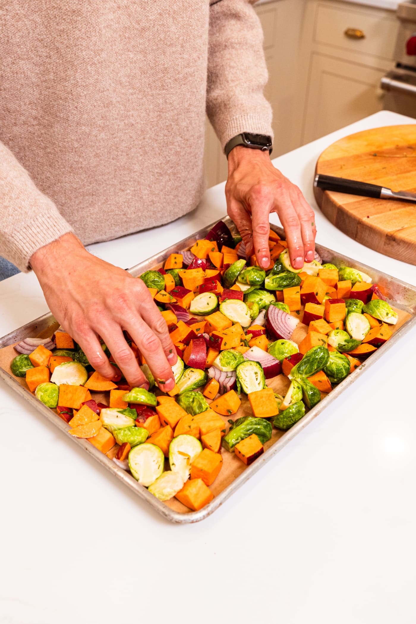Two hands spreading out chopped and diced vegetables on a large sheet pan.