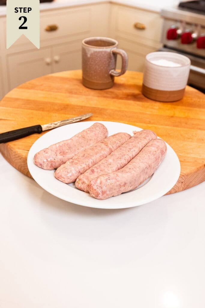 White plate with four large raw sausages sitting on a wooden cutting board.