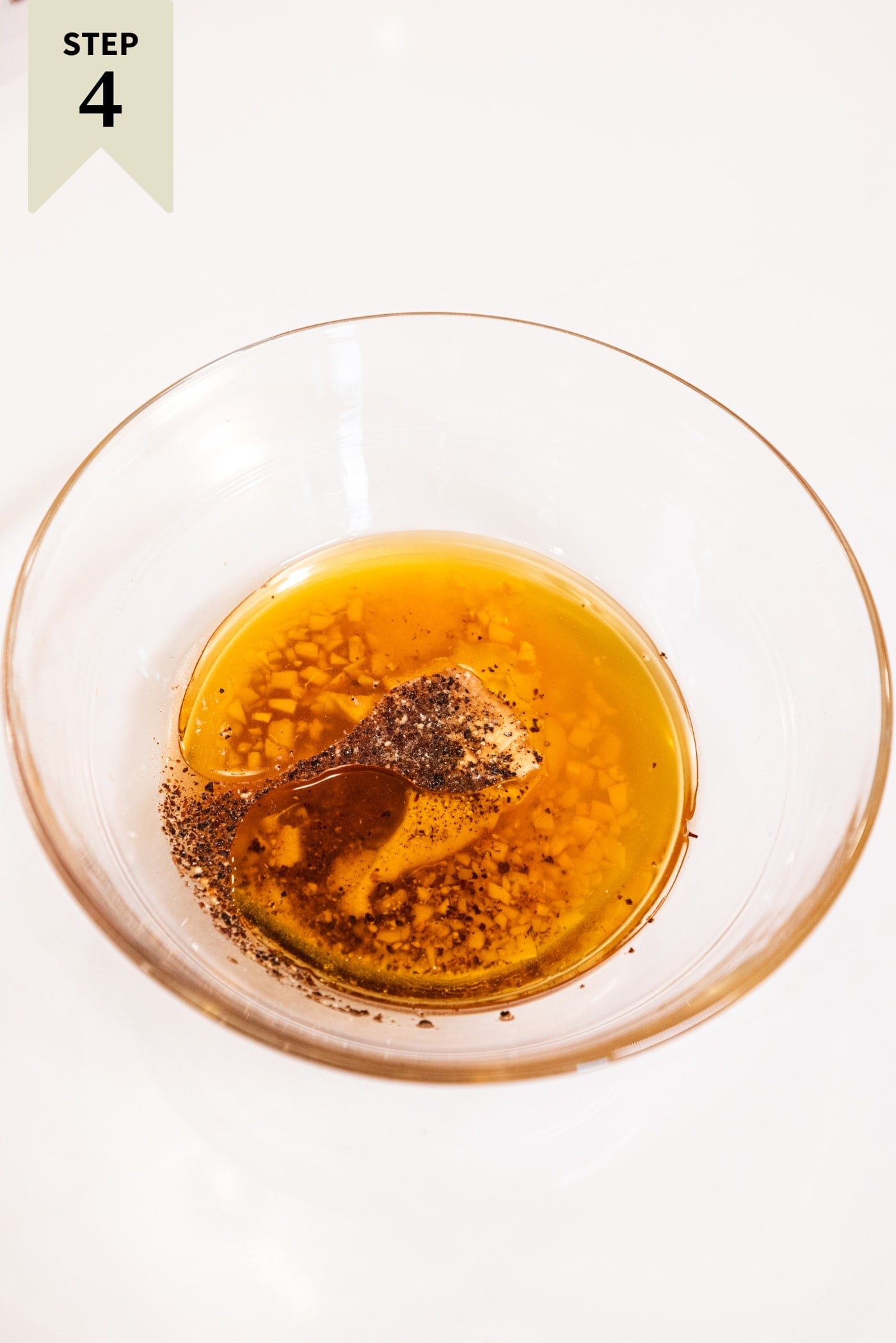 Glass bowl filled with olive oil, Dijon mustard, spices, and more before being mixed together.