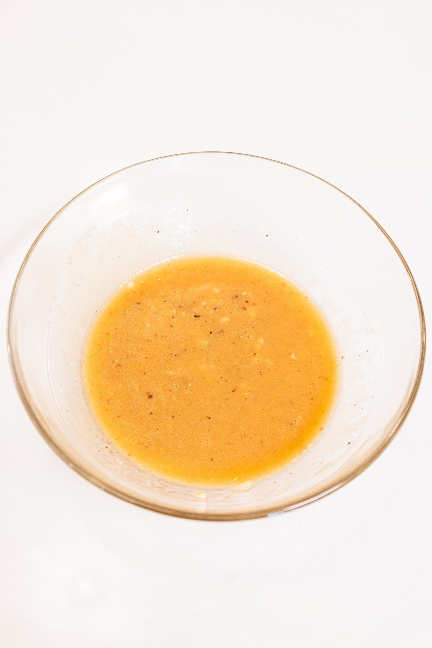 Glass bowl filled with vinaigrette whisked together with a yellow color.