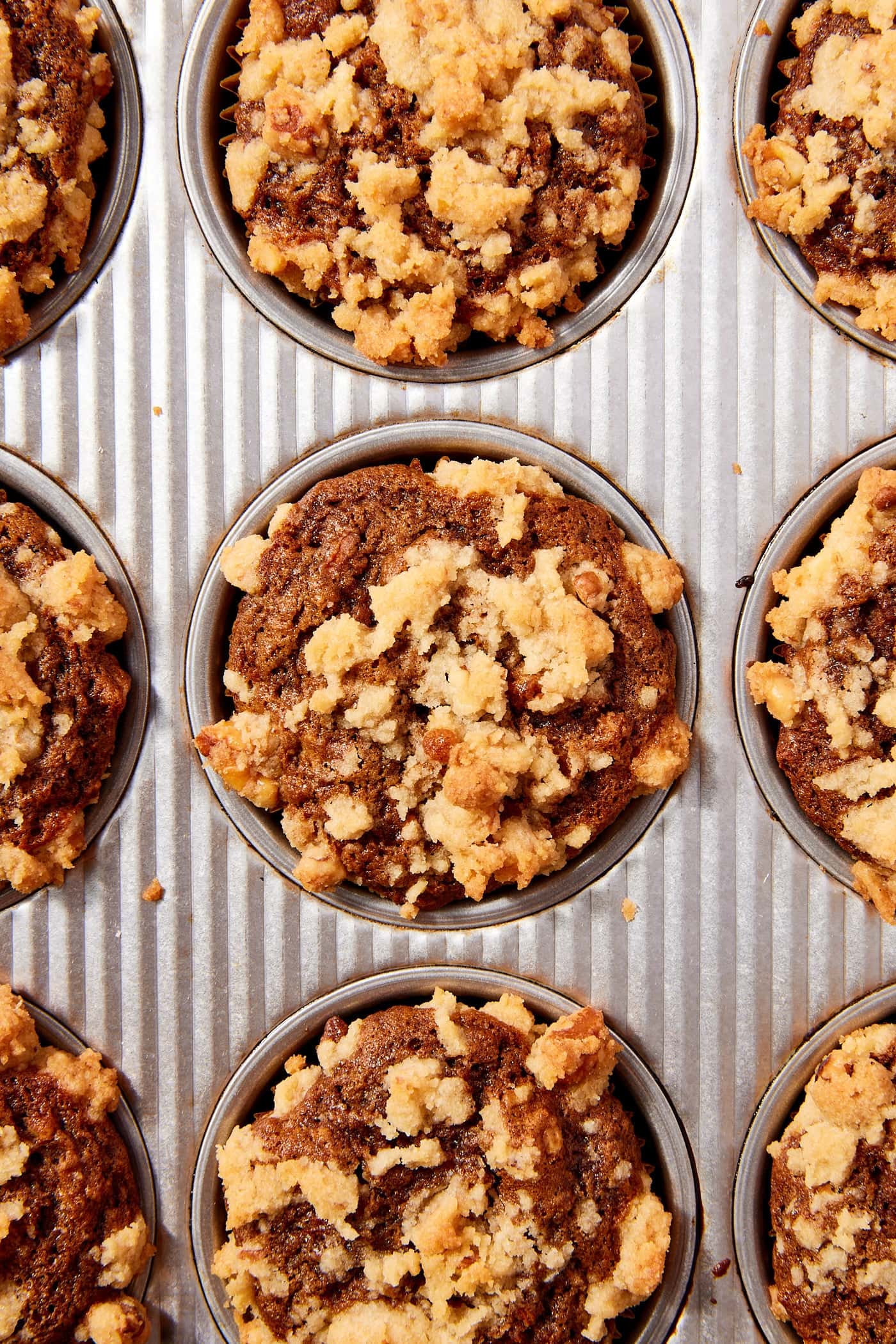 Metal baking pan filled with baked spiced carrot muffins with streusel topping all over.