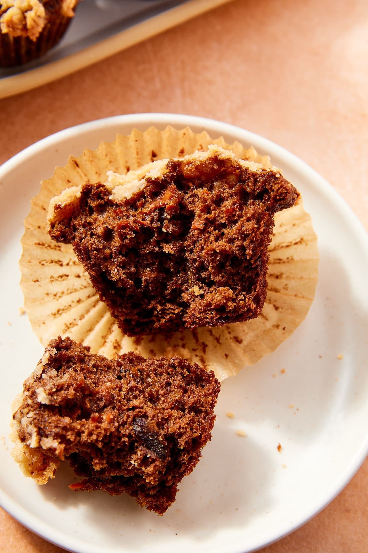 Dark colored spiced carrot muffin with streusel topping resting on plate after being torn in half to show interior.