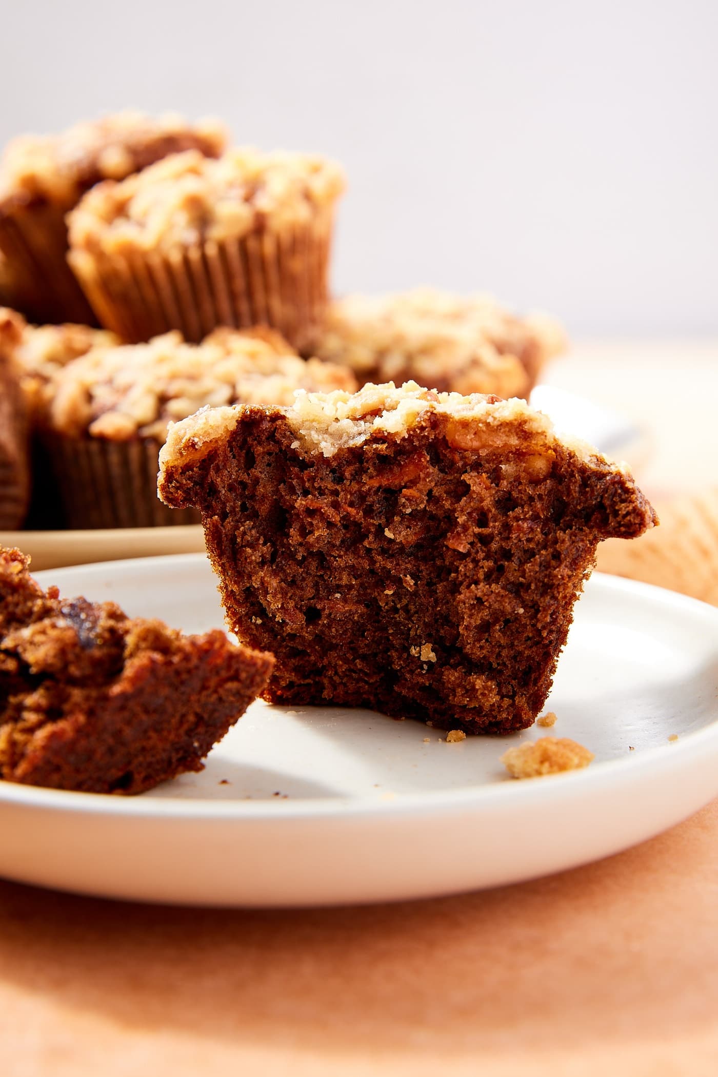 White plate with spiced carrot muffin sitting on it after being broken in half with dark interior texture and streusel topping.