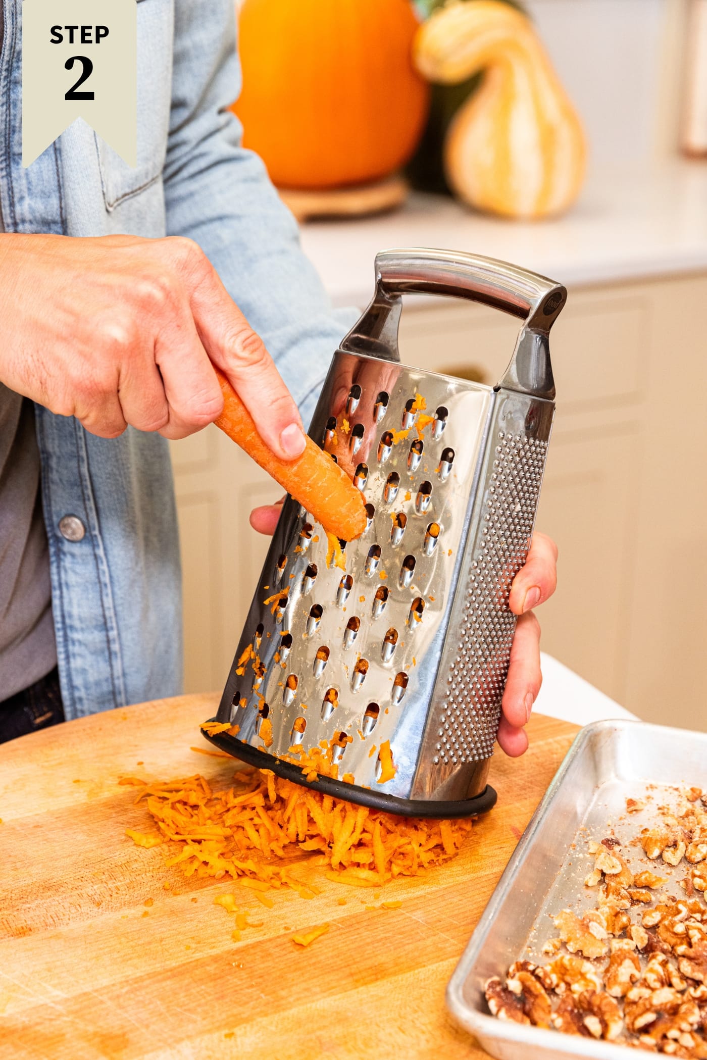 Hand grating carrot on grater onto wood cutting board with pieces of carrot underneath.