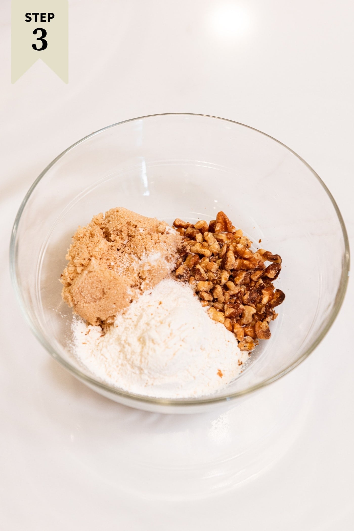 Glass bowl filled with ingredients needed for a streusel topping including brown sugar, white sugar, and nuts.
