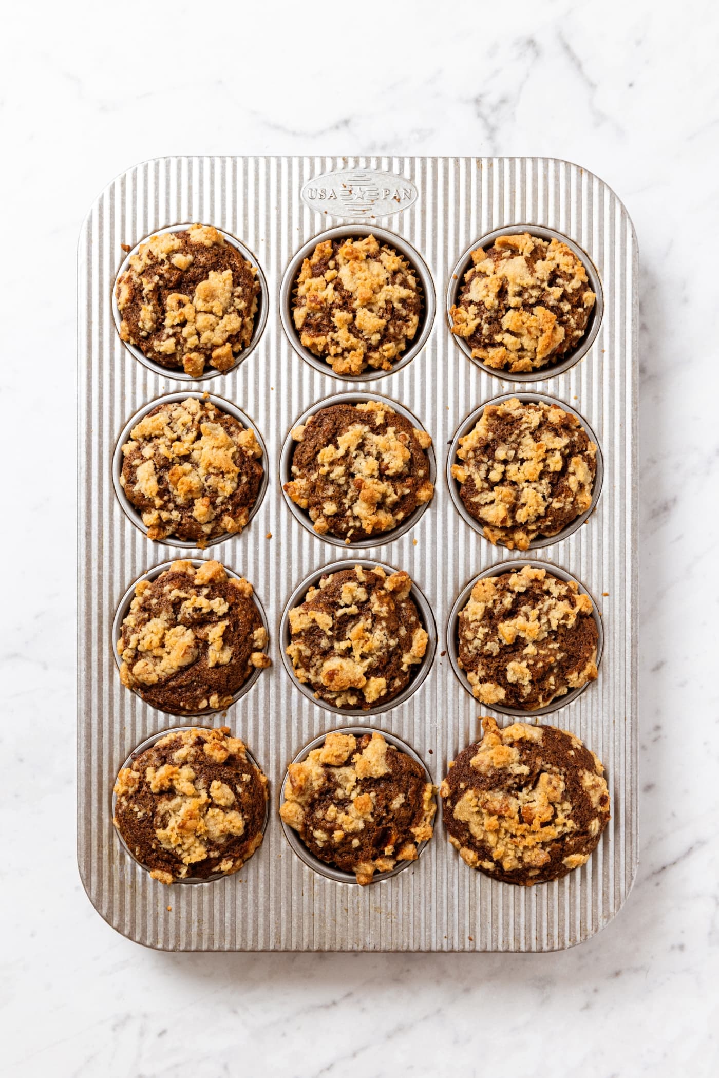 Metal muffin tin on white marble surface with baked spiced carrot muffins right after coming out of the oven.