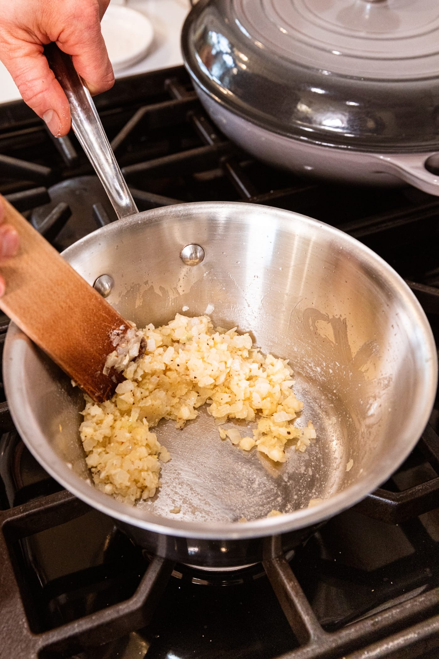 Metal saucepan with wooden spatula mixing together flour mixture with clumps forming.
