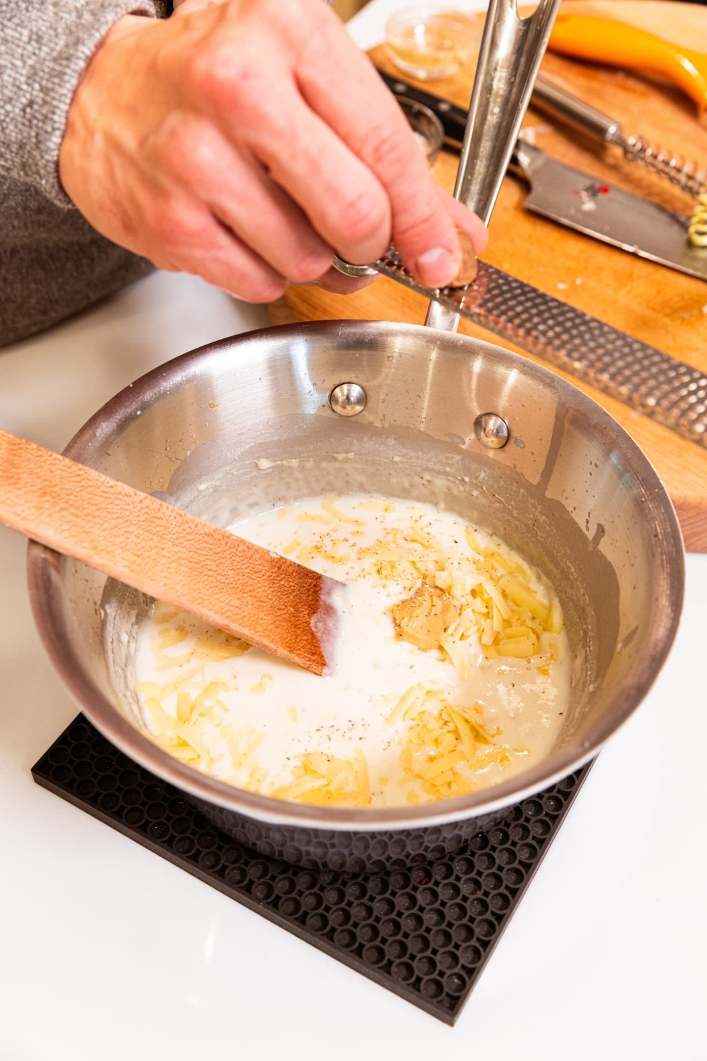 Metal saucepan filled with milk mixture with mustard and more ingredients on top before being mixed together.