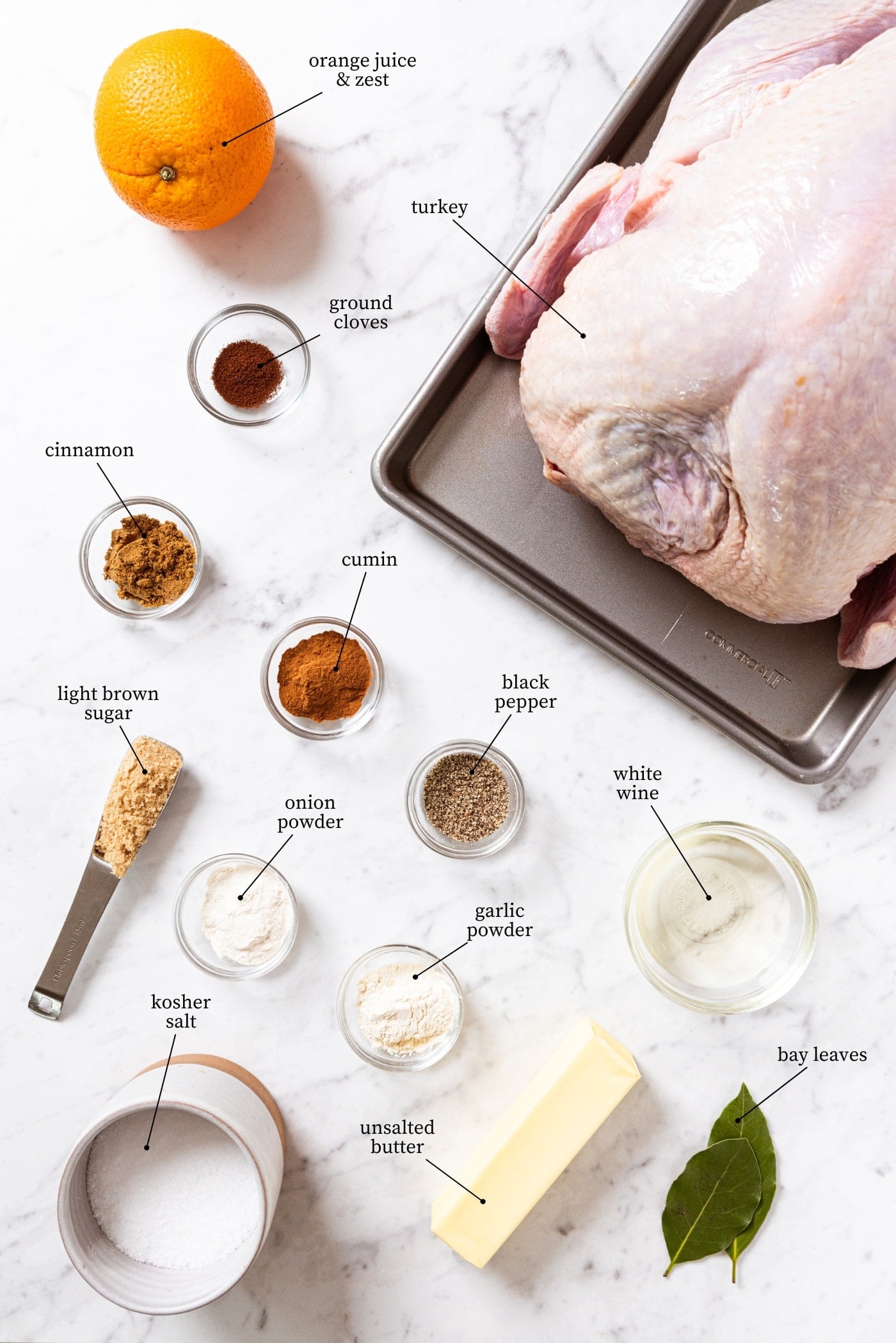 White marble surface filled with all ingredients needed to make an orange spiced turkey including raw turkey, spices, sugar, white wine, and more.