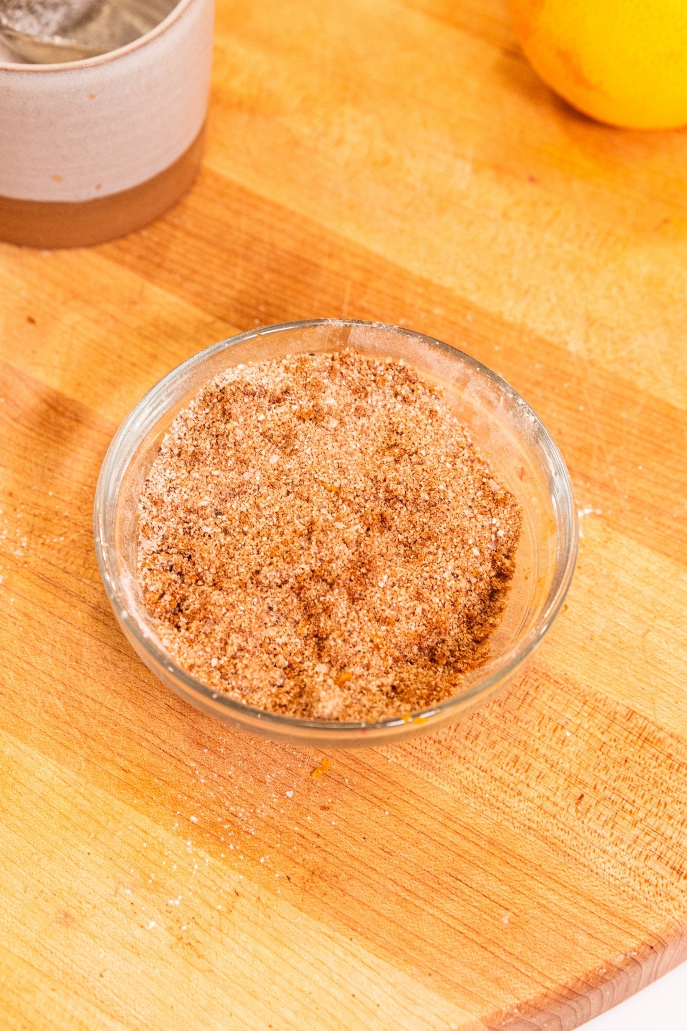 Small glass bowl filled with mixture of dry brine to be sprinkled over top of a raw turkey all on wooden cutting board.