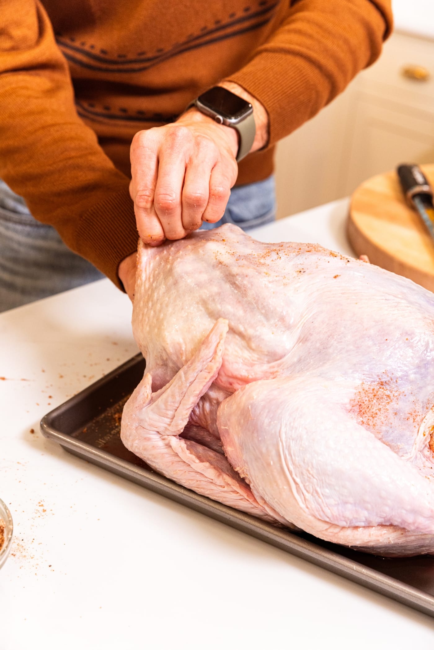 Hands holding back the skin of a raw turkey using hand to break the skin away from the meat.