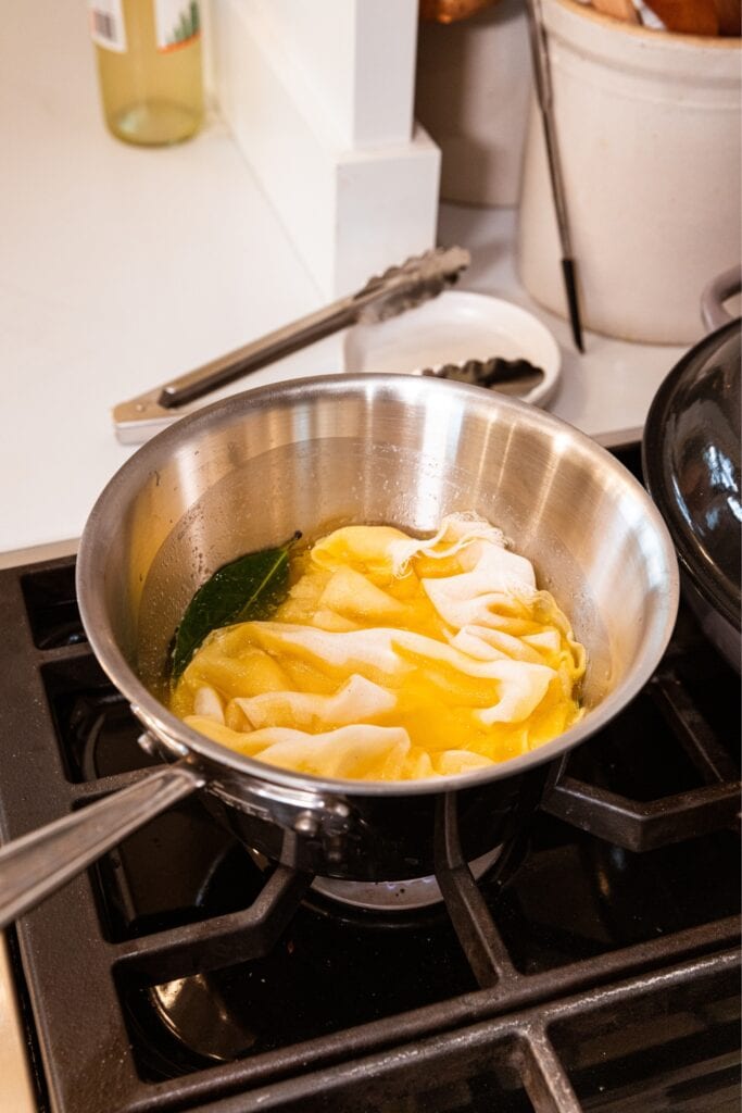 Metal saucepan sitting on a stovetop with cheesecloth soaking into a white wine and butter mixture.