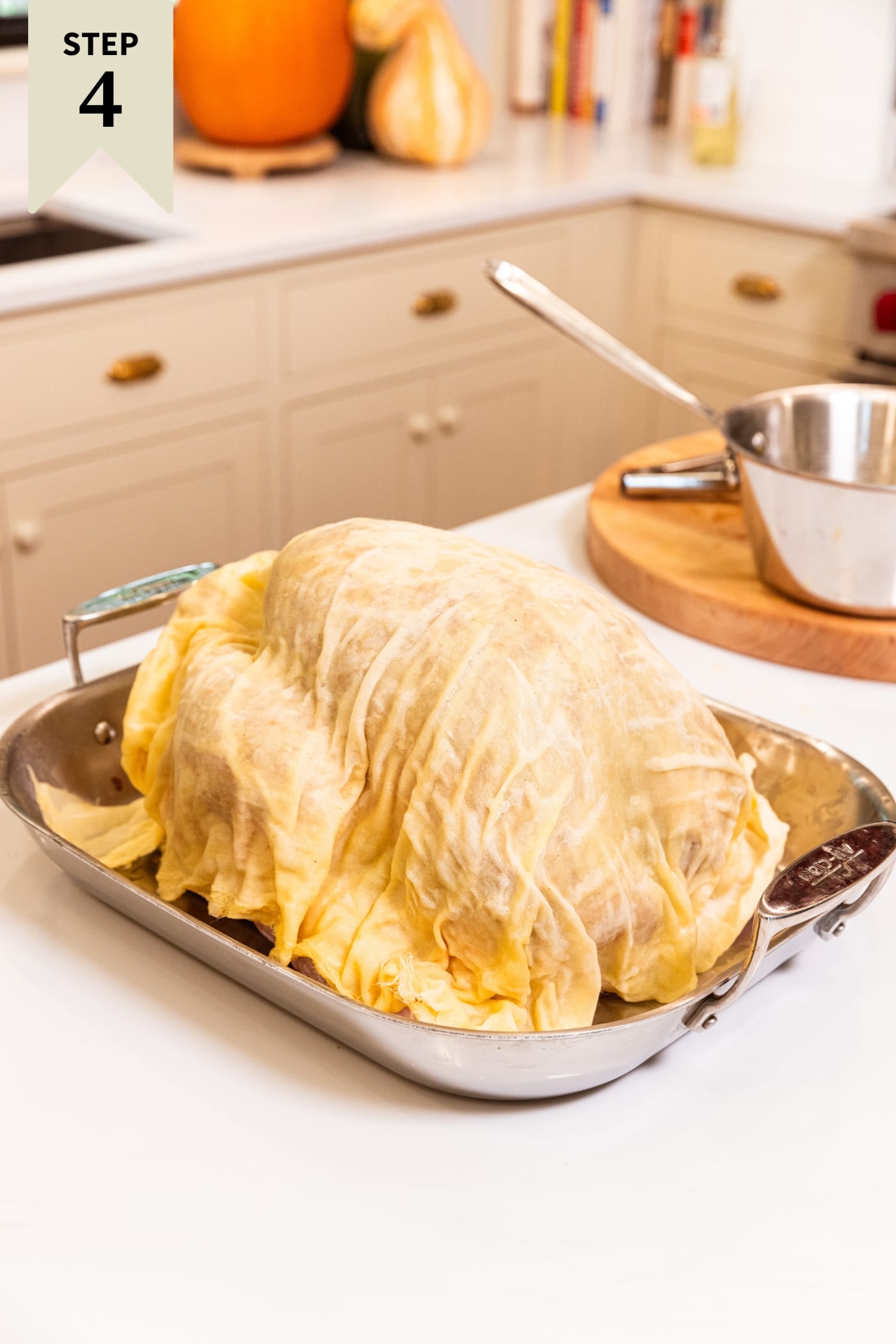Cheesecloth soaking in basting liquid draped over the top of a large Thanksgiving turkey in a roasting pan.