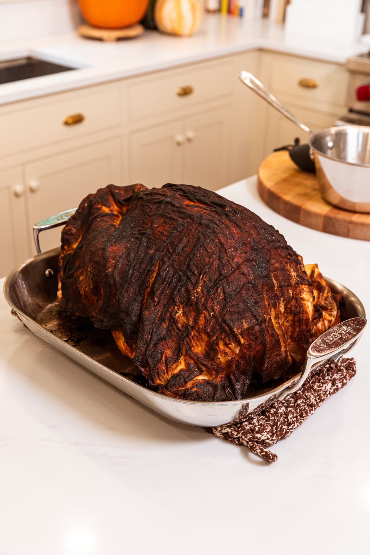 Large turkey in a metal pan with browned cheesecloth after roasting in the oven.