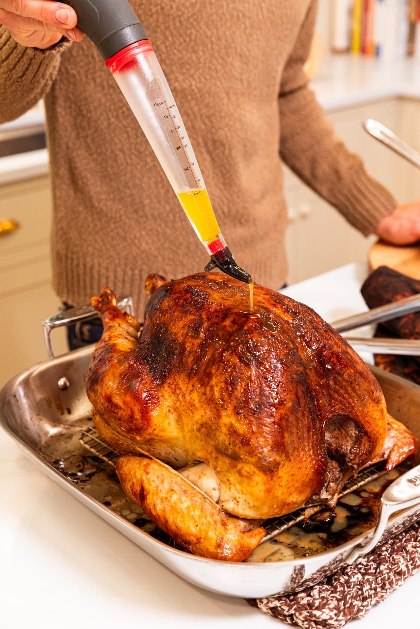 Hand using a turkey baster to baste a large golden Thanksgiving turkey with butter and white wine mixture.