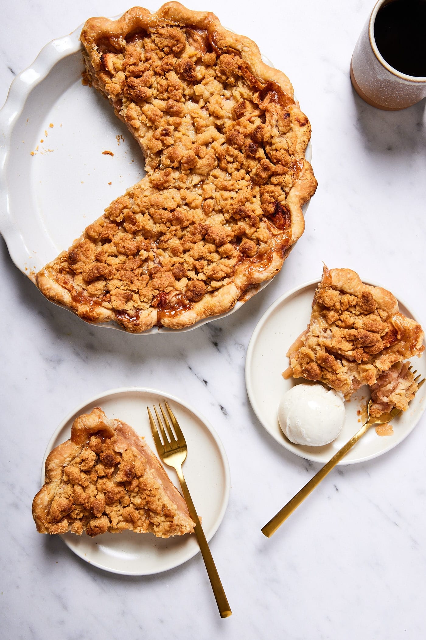 Classic apple pie with two slices removed sitting on plates one with ice cream and rest of the pie to the side.