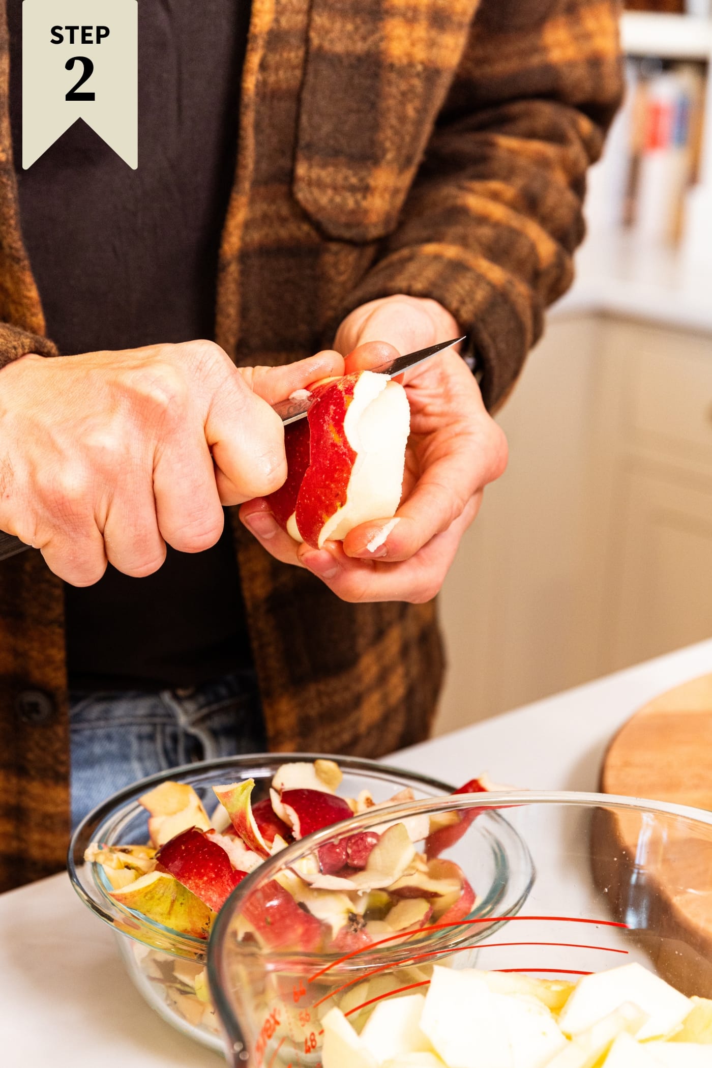 Hand using the back of a knife to peel apples into a large measuring cup.