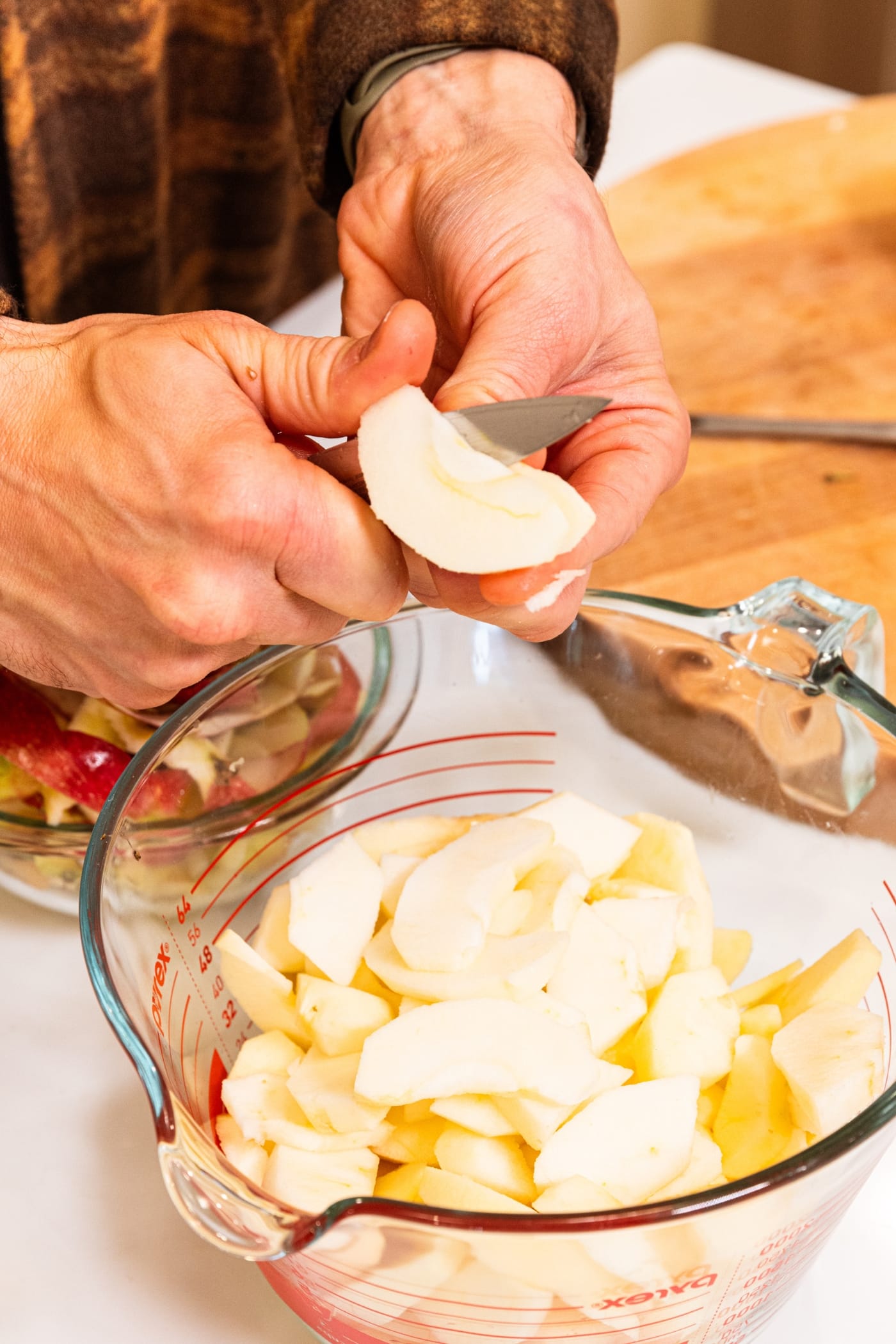 Hand using knife to slice apples into a large measuring cup in the kitchen.