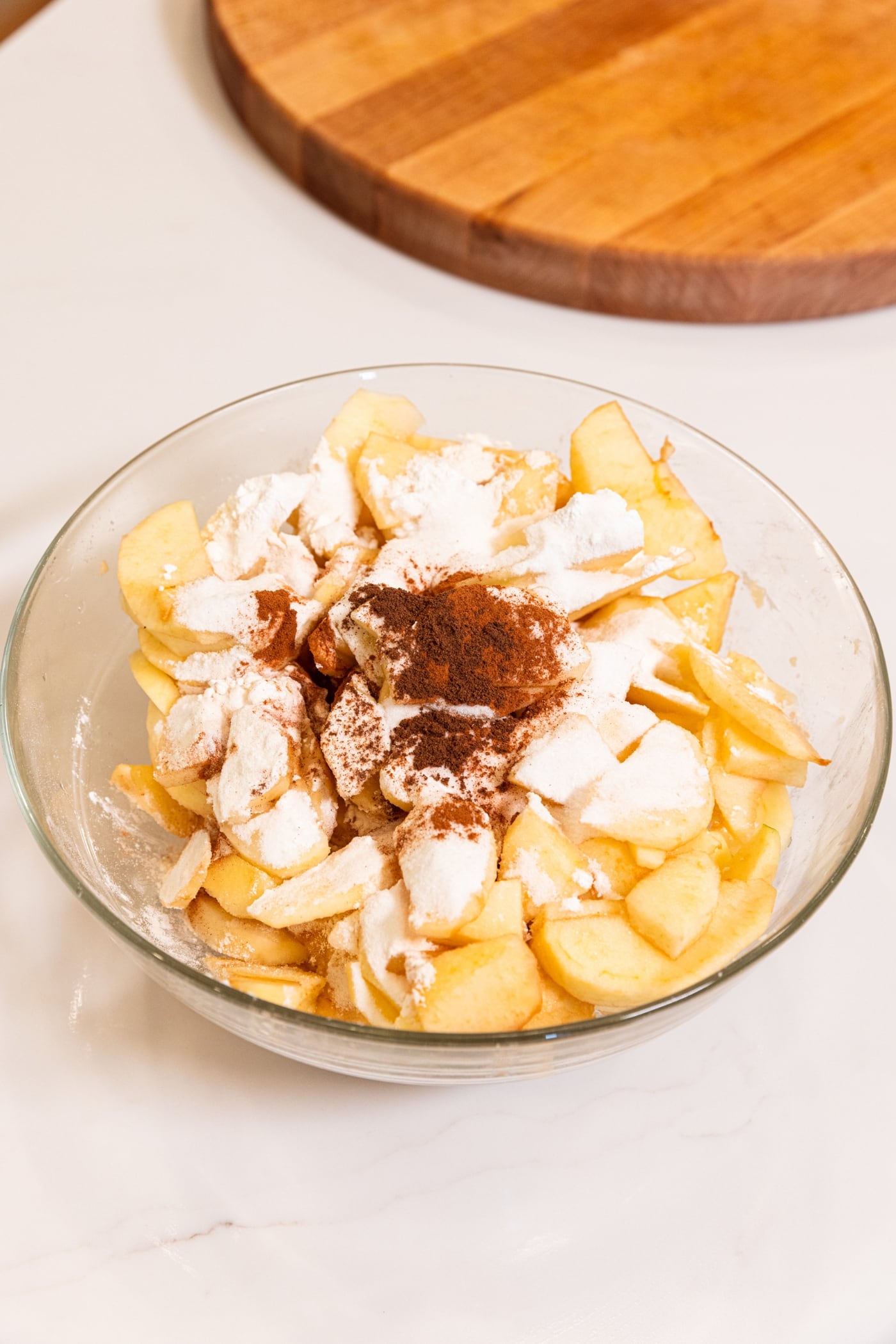 Glass bowl filled with sliced apples with cinnamon and white sugar all over the top before being mixed together.