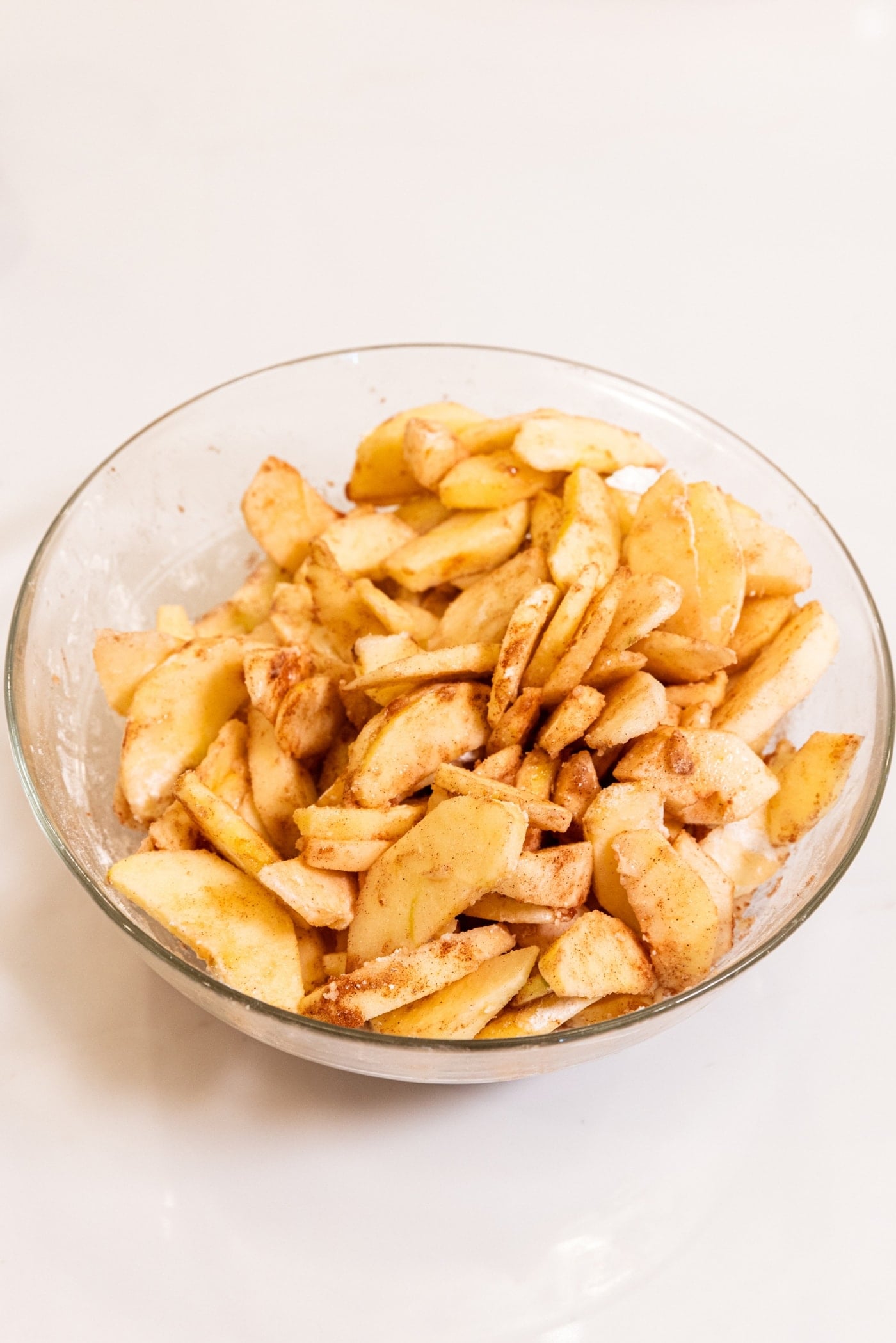Glass bowl filled with sliced apples with cinnamon and sugar mixture all over.