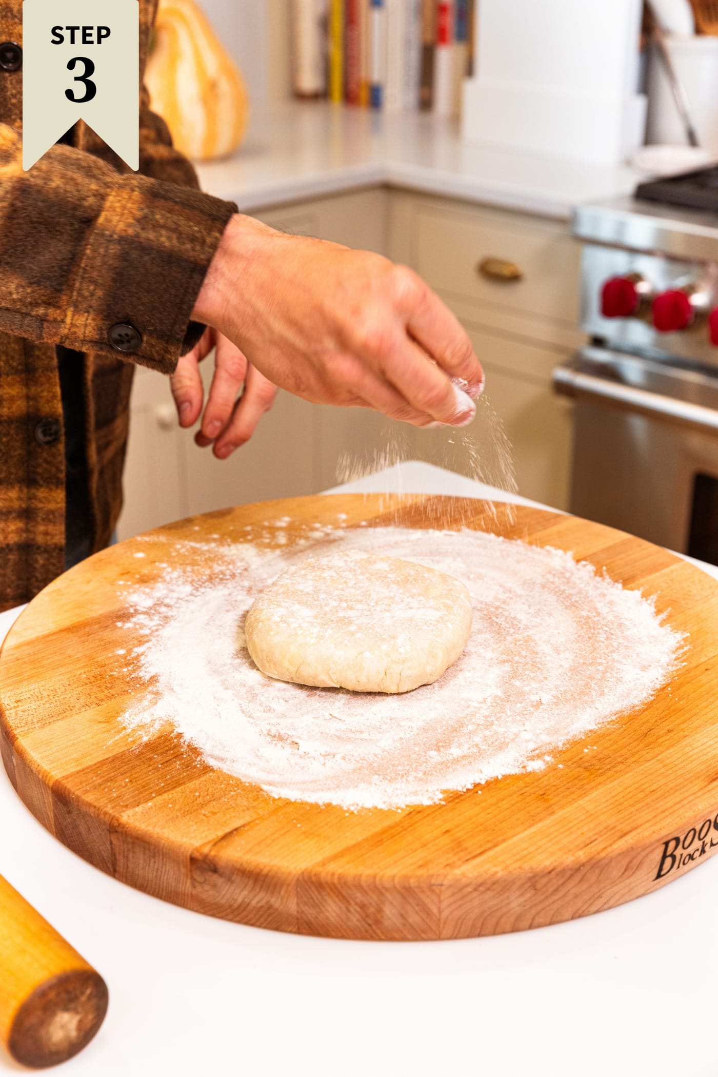 Hand sprinkling flour on top of a cold round of pie dough on a cutting board.