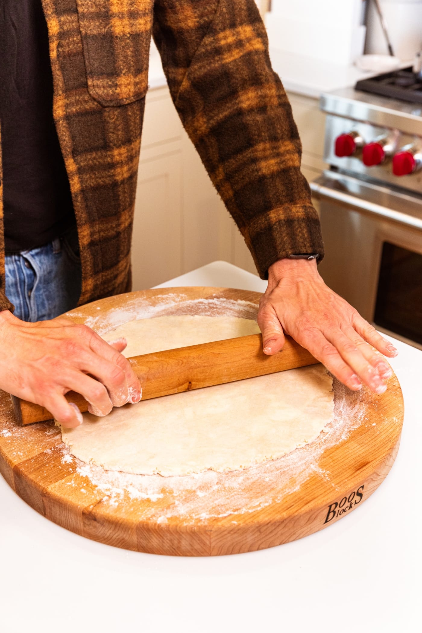 Hands using a wooden rolling pin to roll out a pie crust to a thin thickness on wooden cutting board.