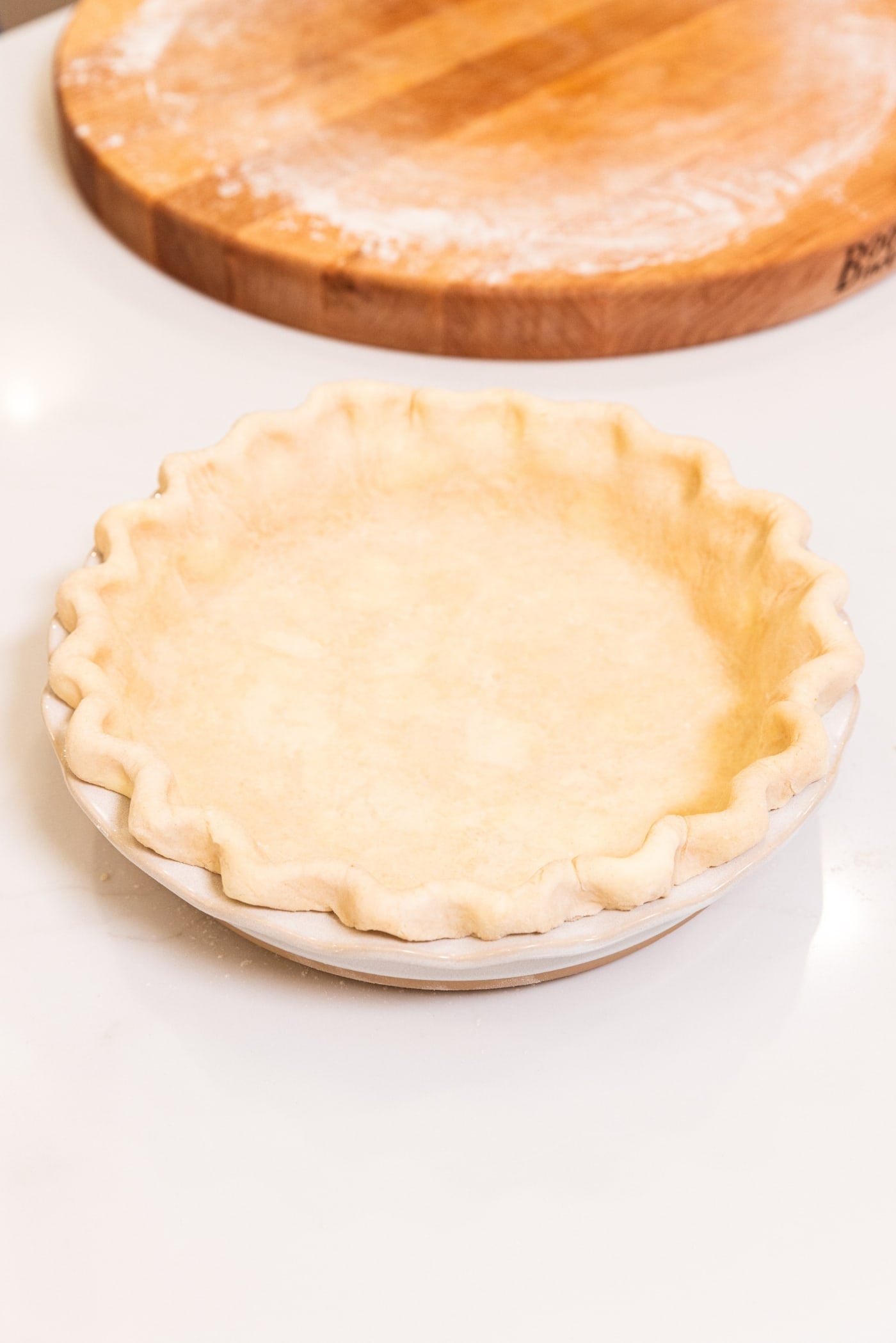 A pie crust resting in a white baking dish after being crimped and before being filled.