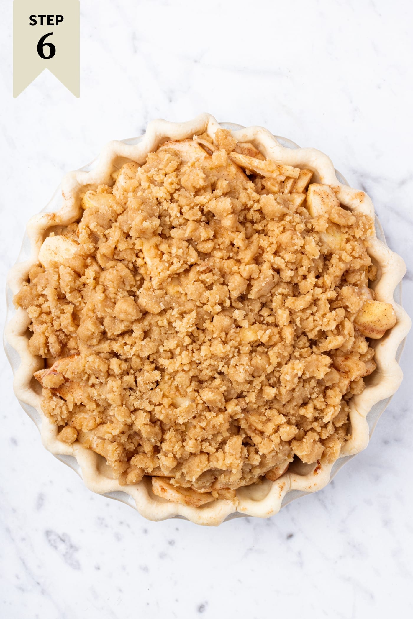 White marble surface with unbaked classic apple pie with streusel topping right before going into the oven to bake.