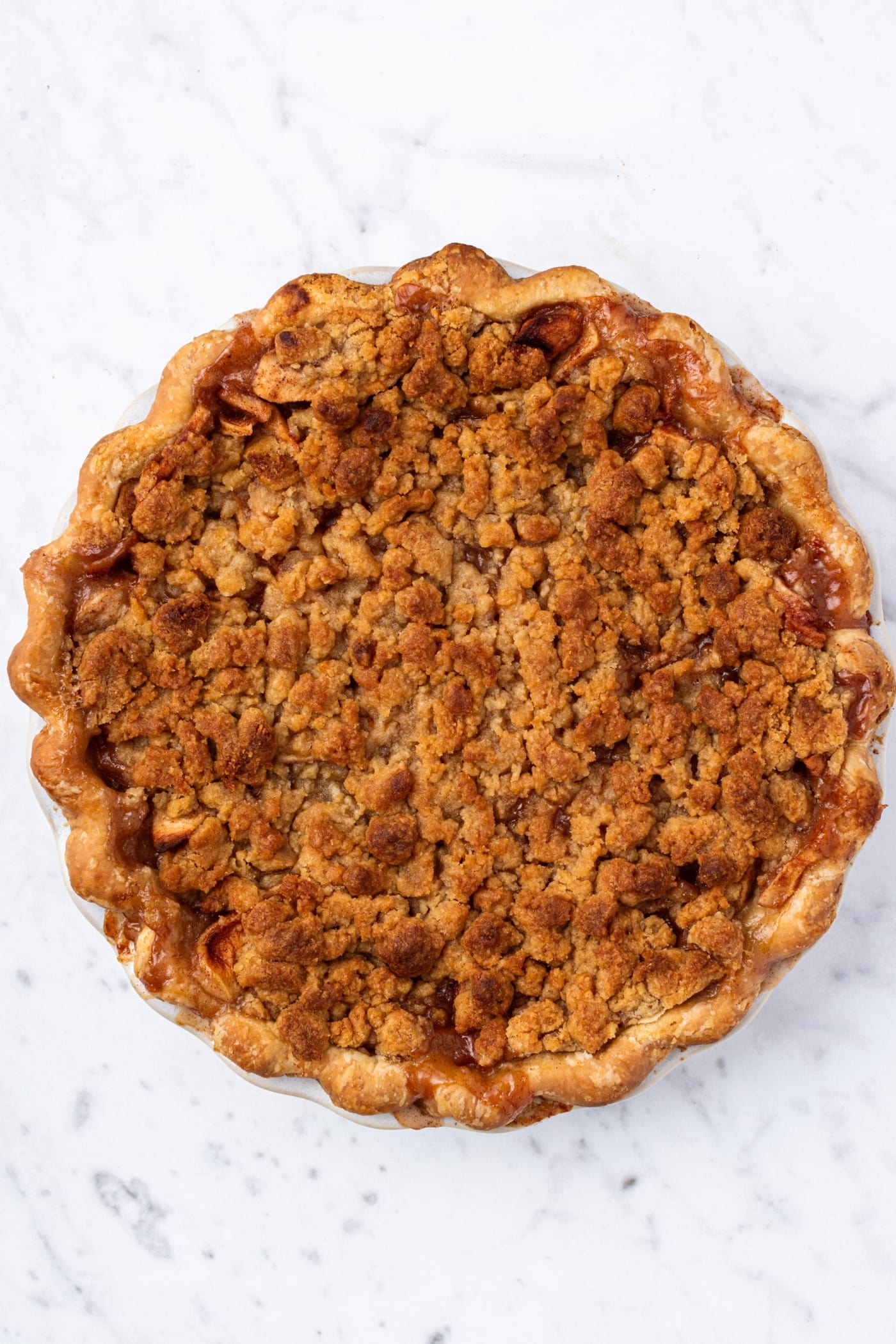 White marble surface with fully baked classic apple pie right after coming out of the oven.